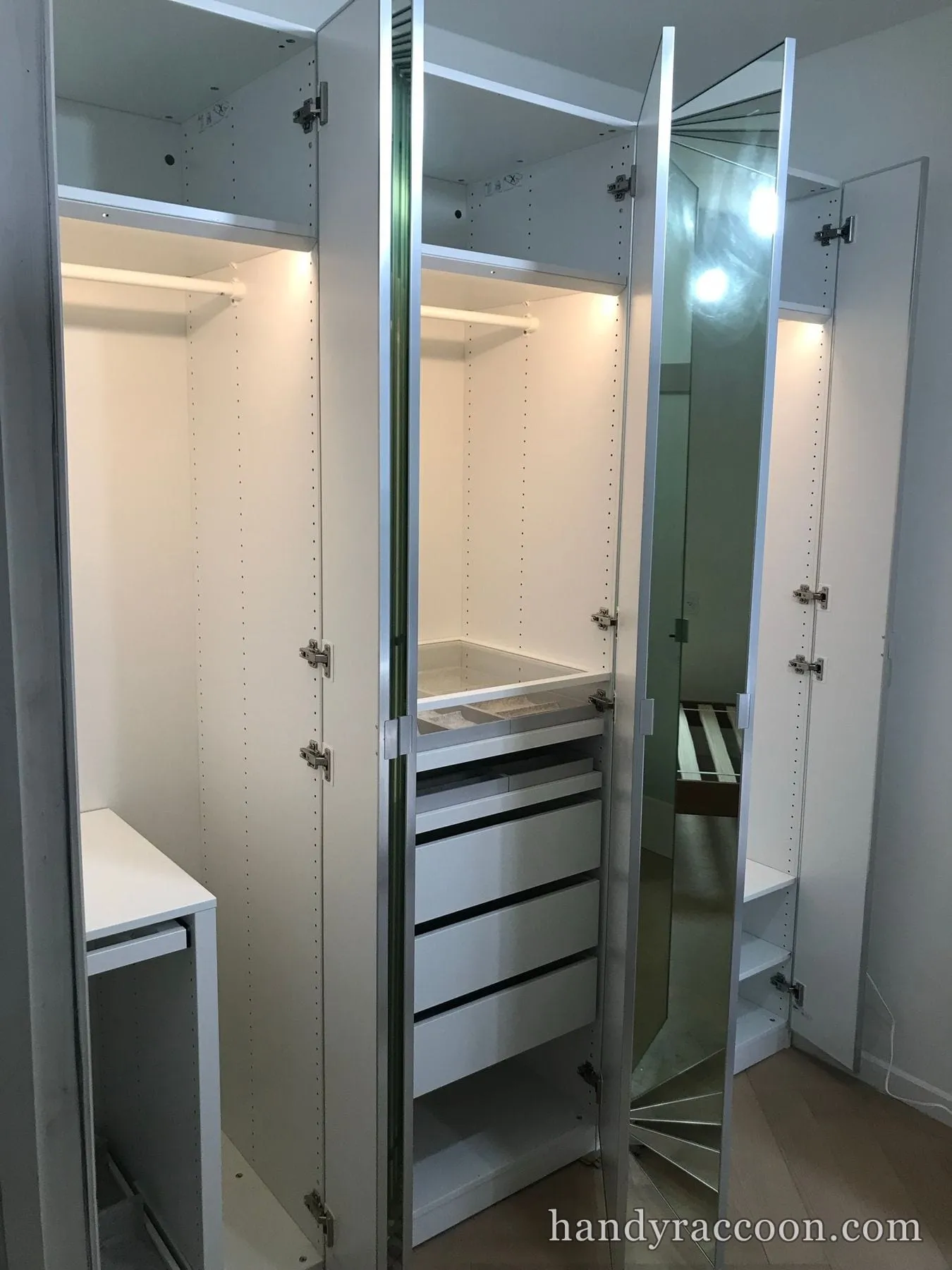 Open white wardrobes with clothes rails, stacked drawers and a mirrored door under strip lighting