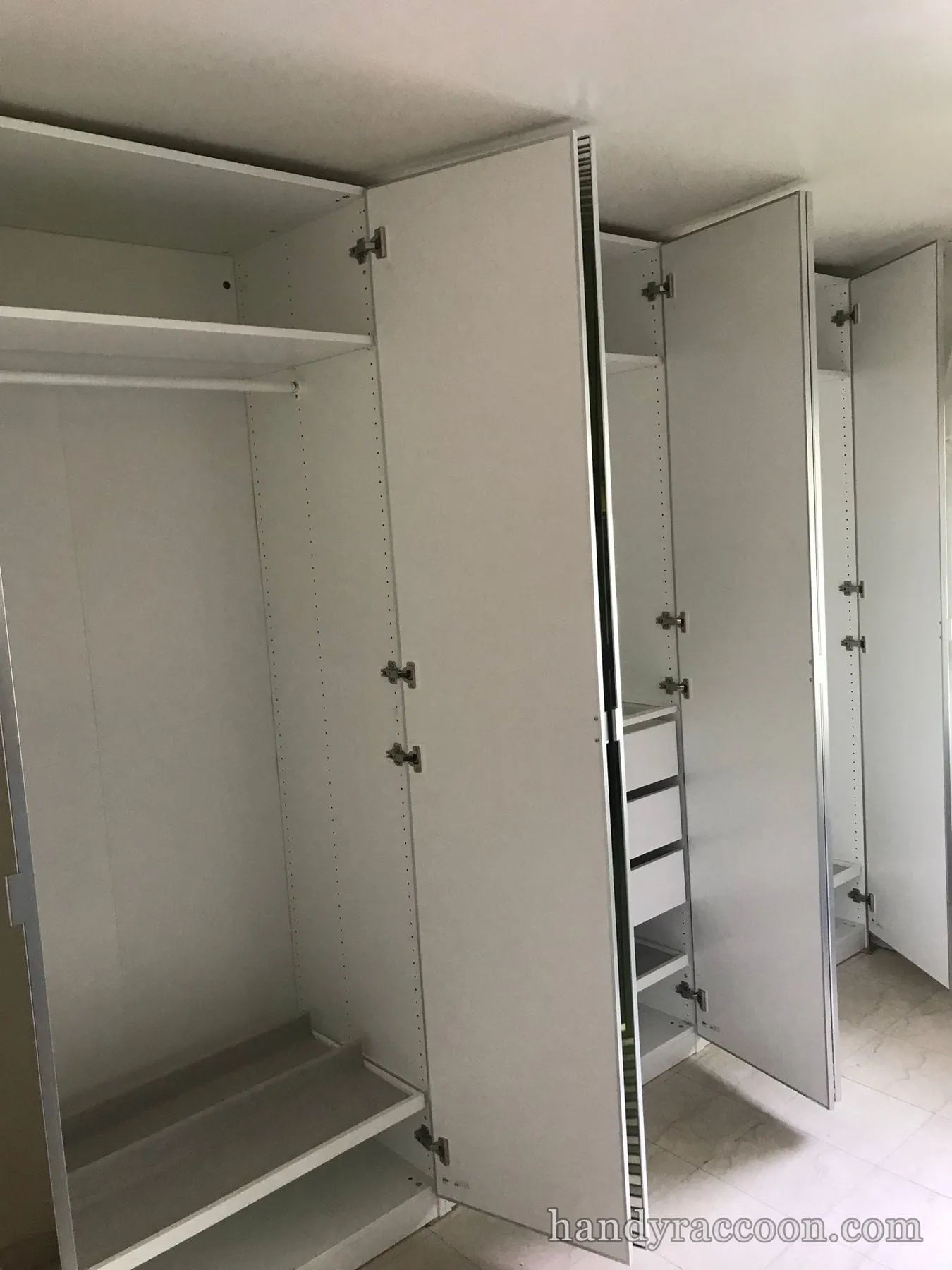 Several tall white wardrobe units with doors open showing empty shelves and drawers on tile