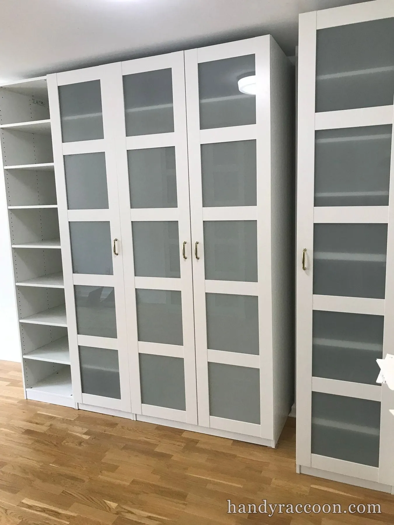 Tall white wardrobes with frosted-glass panel doors and brass handles next to an open bookshelf