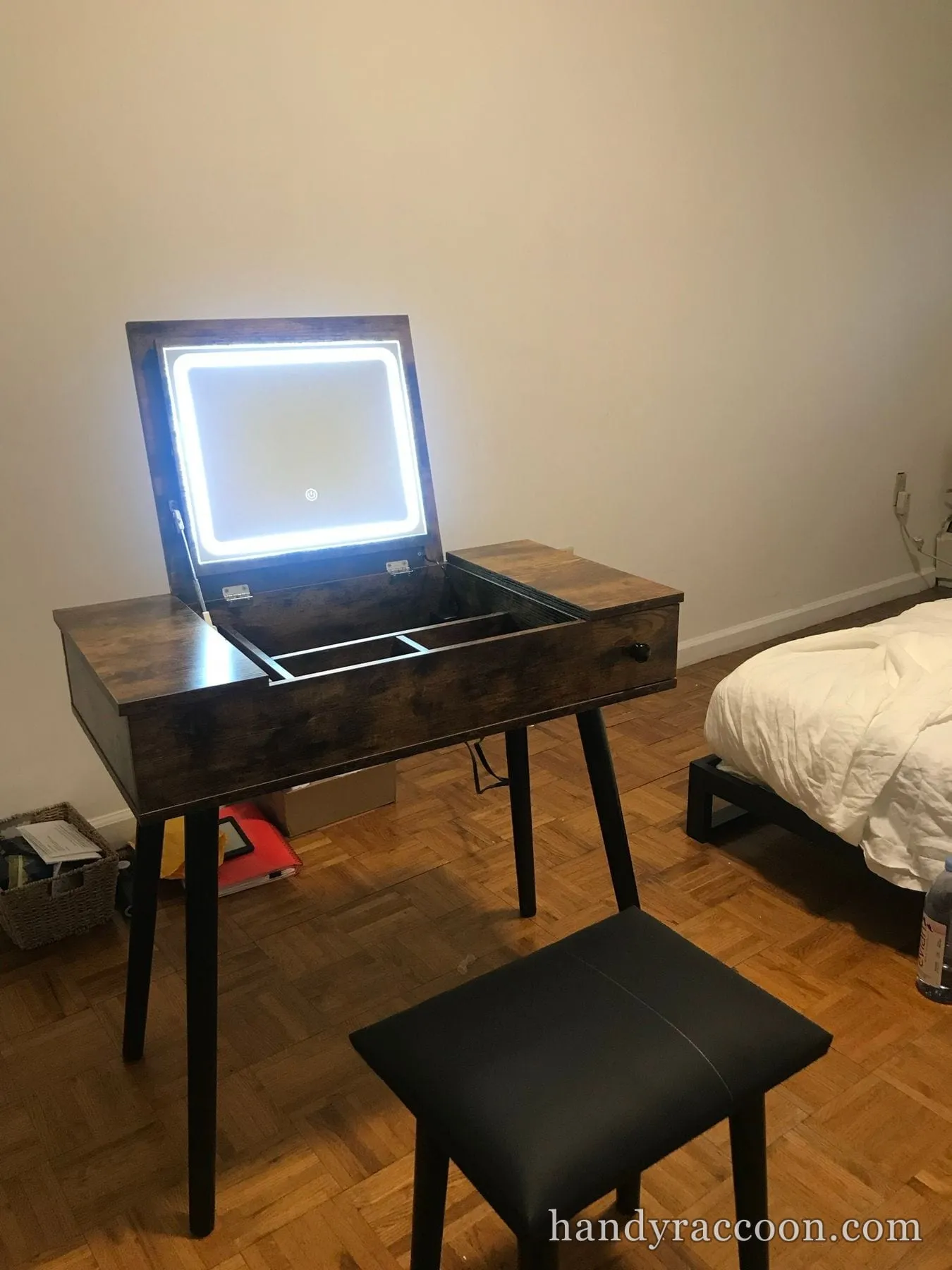 Dark wood vanity desk with a lit flip-up mirror and black stool assembled in a bedroom.