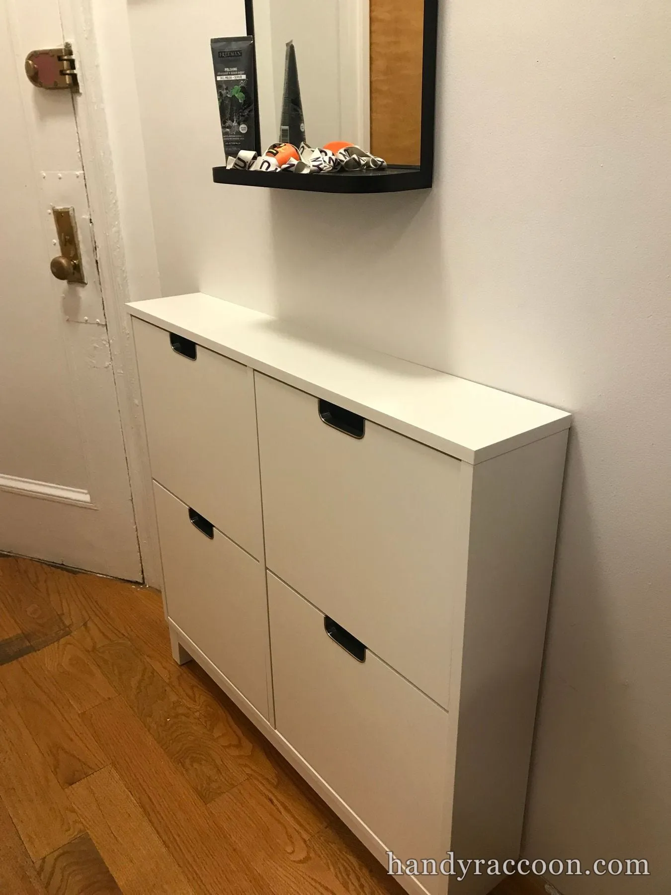 Narrow white shoe storage cabinet with tilt drawers assembled against a hallway wall near a door.