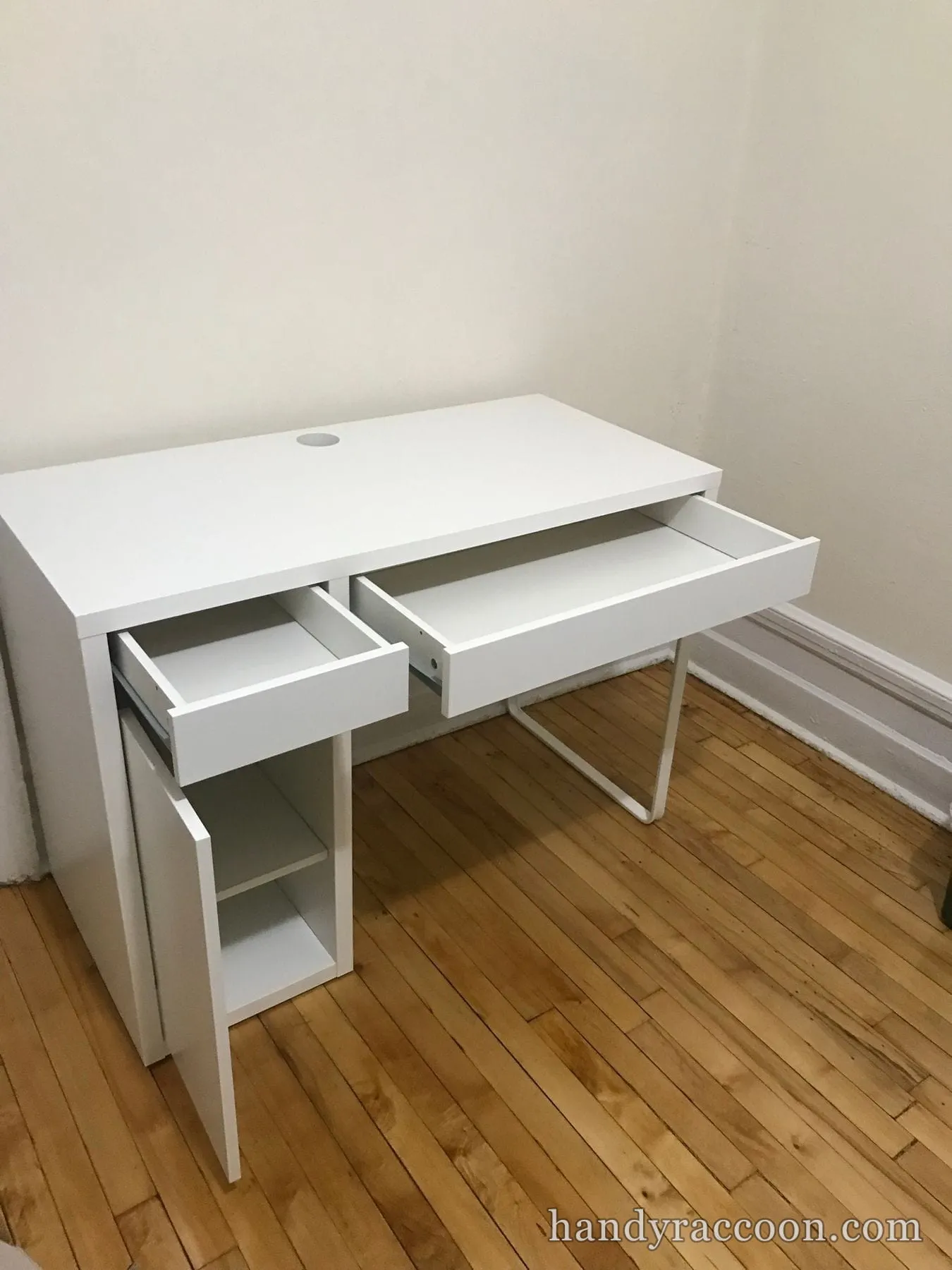 Compact white desk with two open drawers and an open side cabinet on a wood floor.
