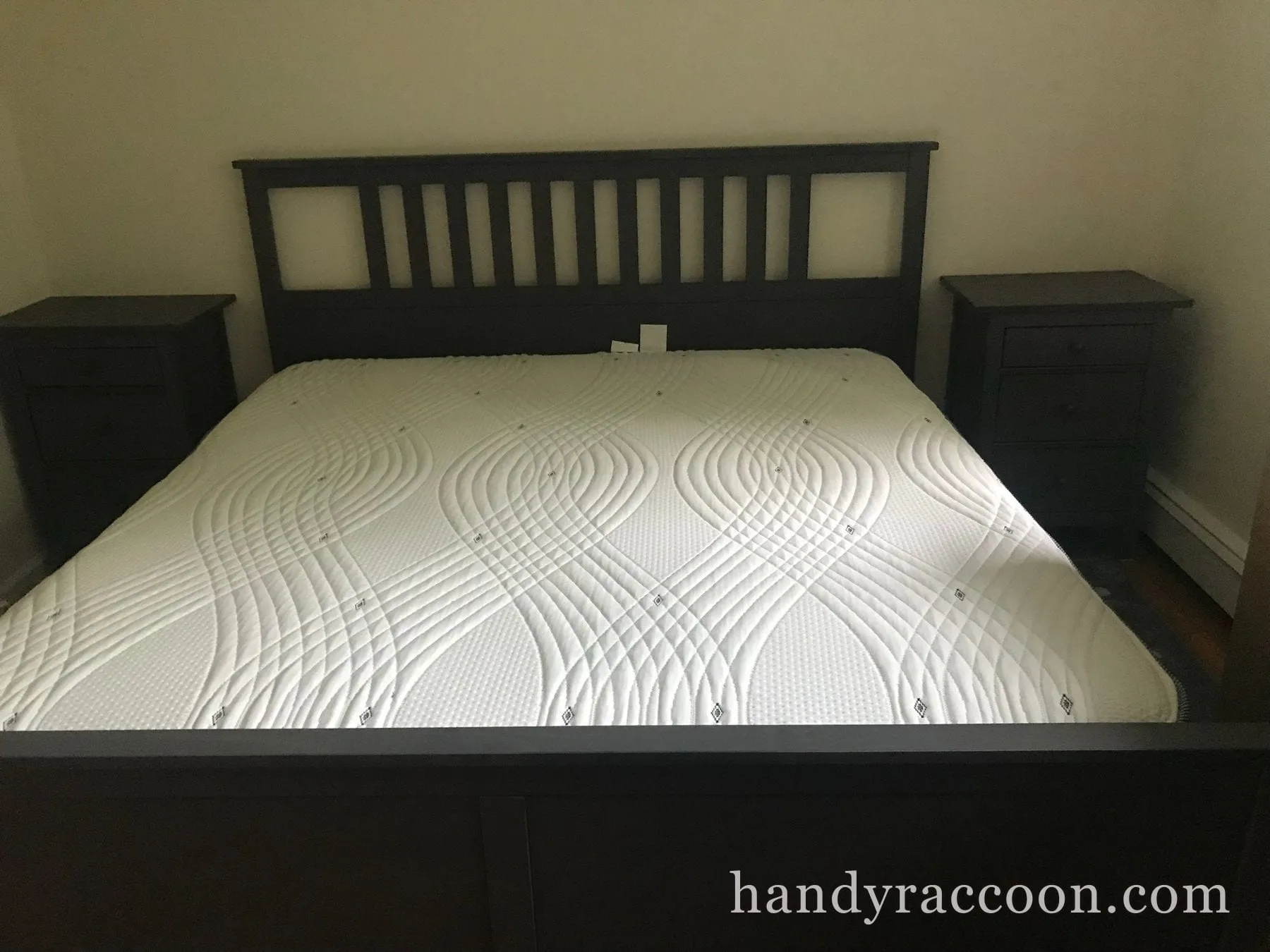 Grey wood bed frame with mattress flanked by two matching nightstands in a bedroom.