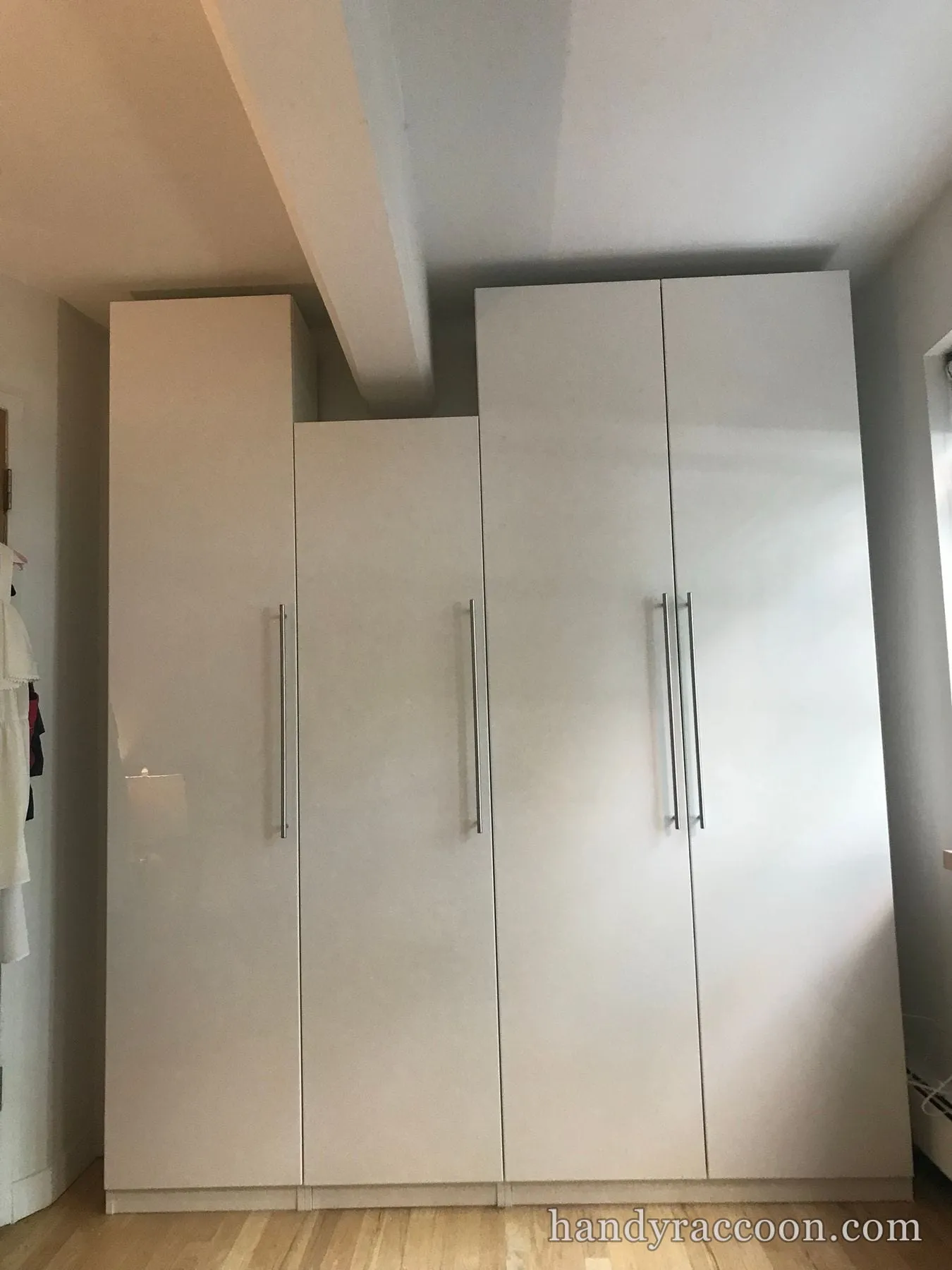 Four tall beige wardrobes with long handles assembled side by side against a bedroom wall.