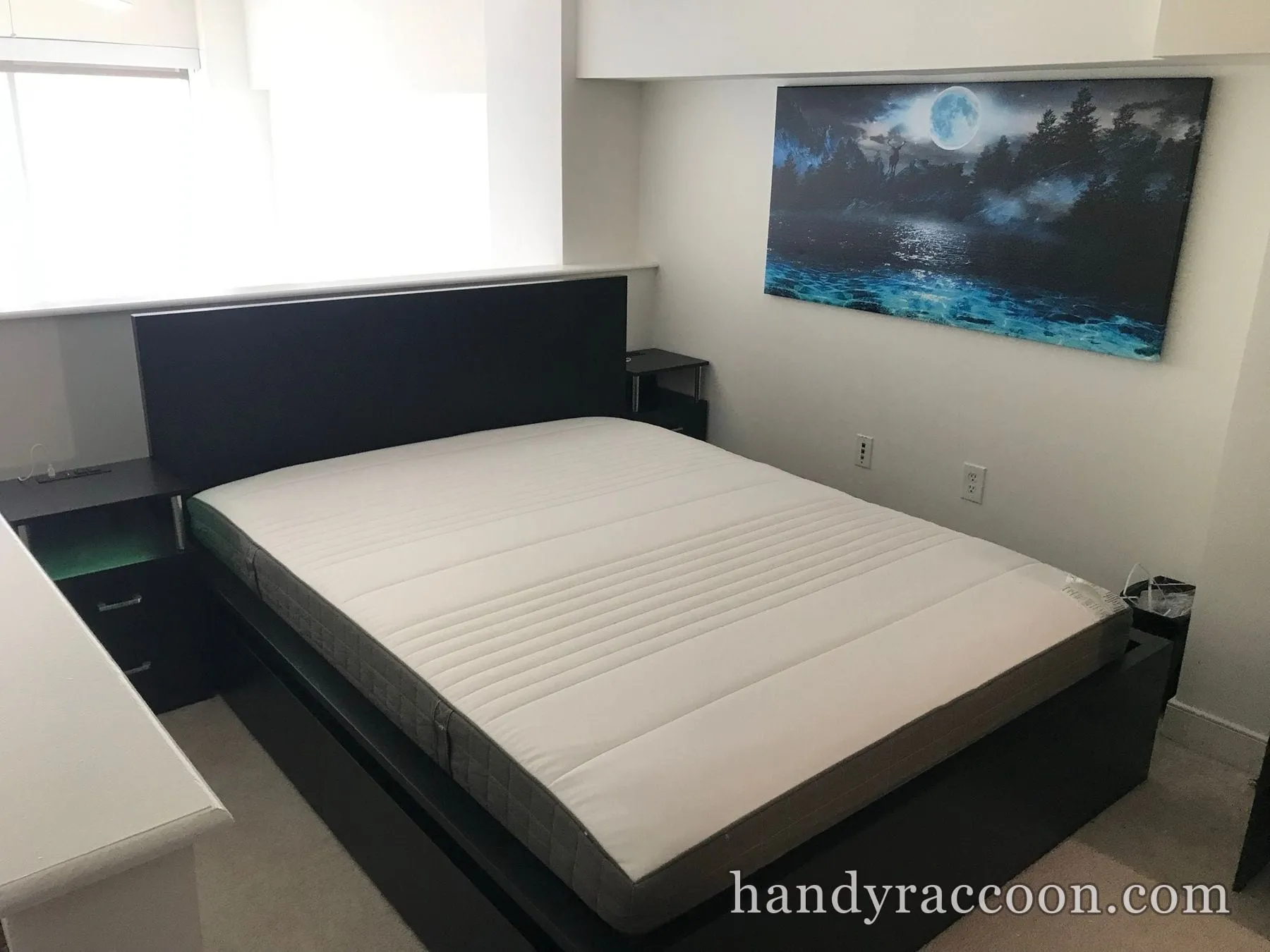 Black platform bed with a white mattress and matching nightstands assembled under a wall canvas.