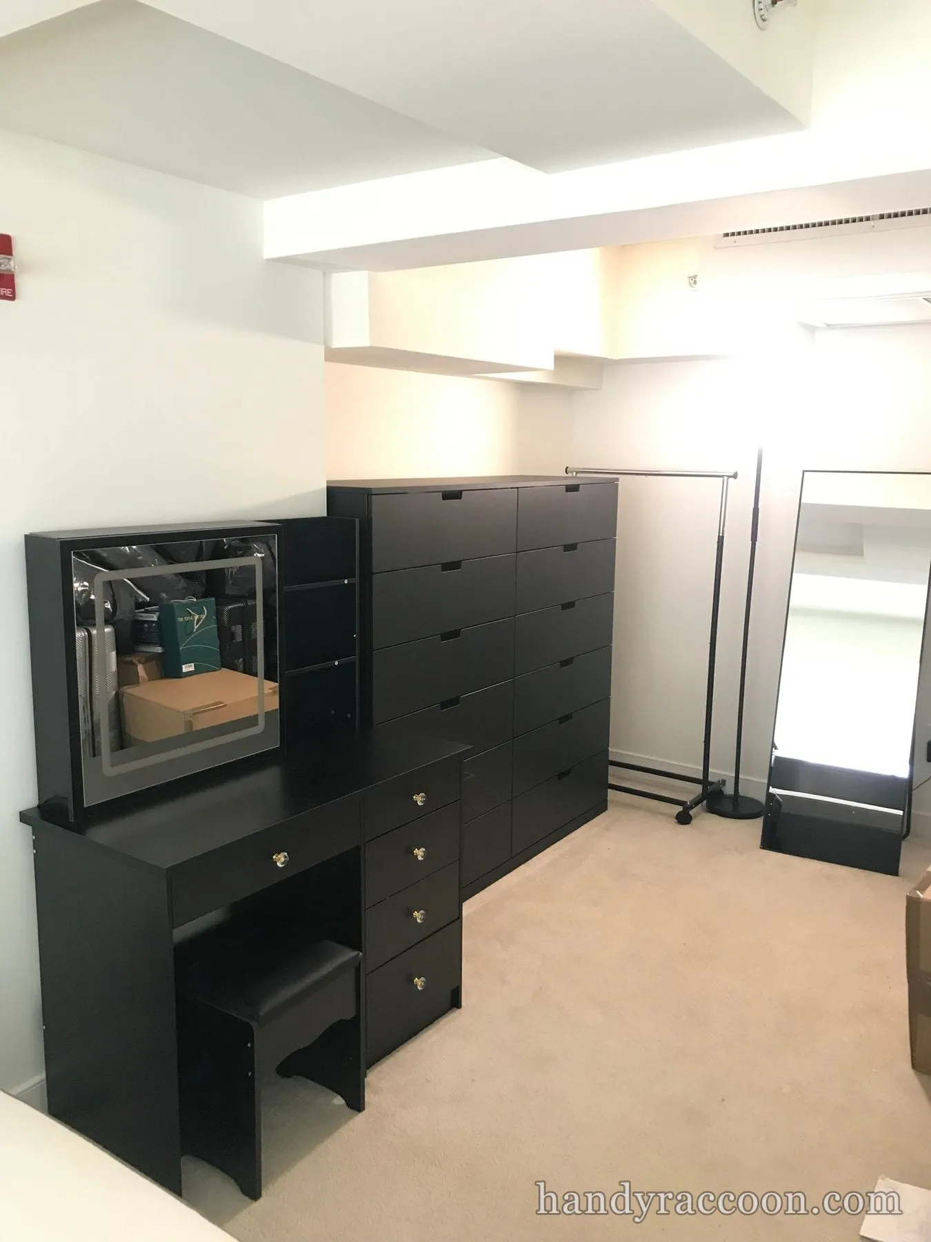 Black vanity with mirror, two chests of drawers, stool, and standing mirror assembled in a room.