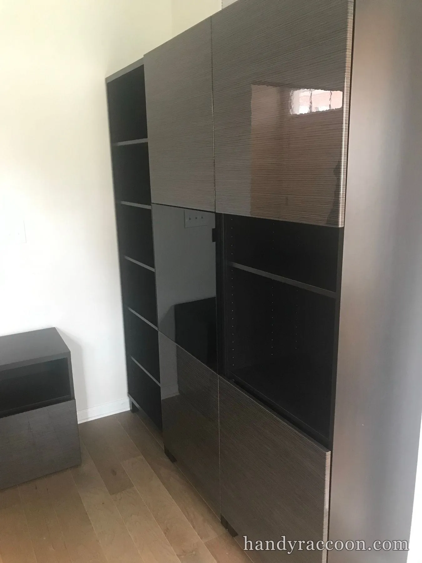 Assembled dark brown storage cabinet system with glossy doors and open shelf sections against a wall.