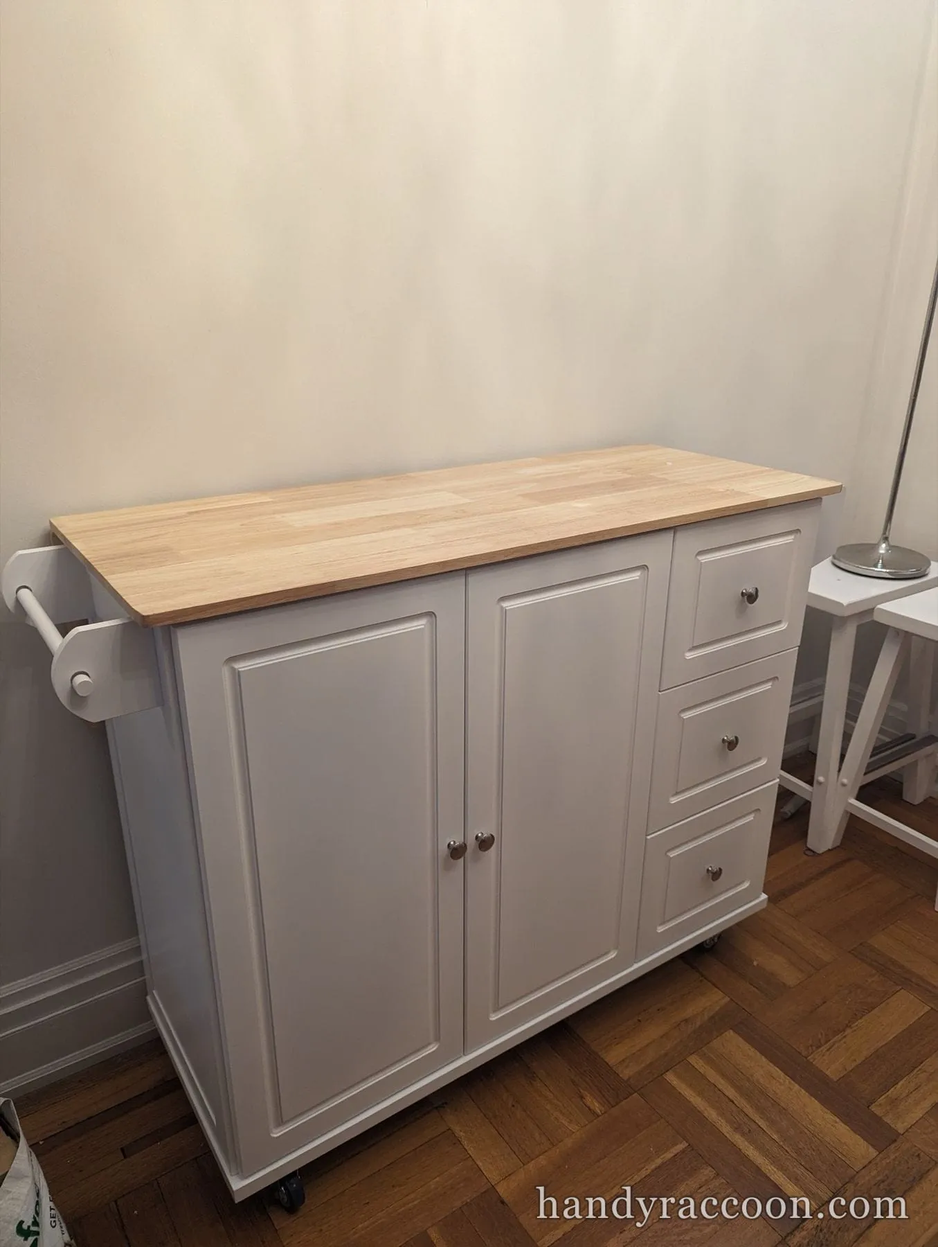 White rolling kitchen island cart with a butcher-block-style wood top, cabinet doors and drawers.
