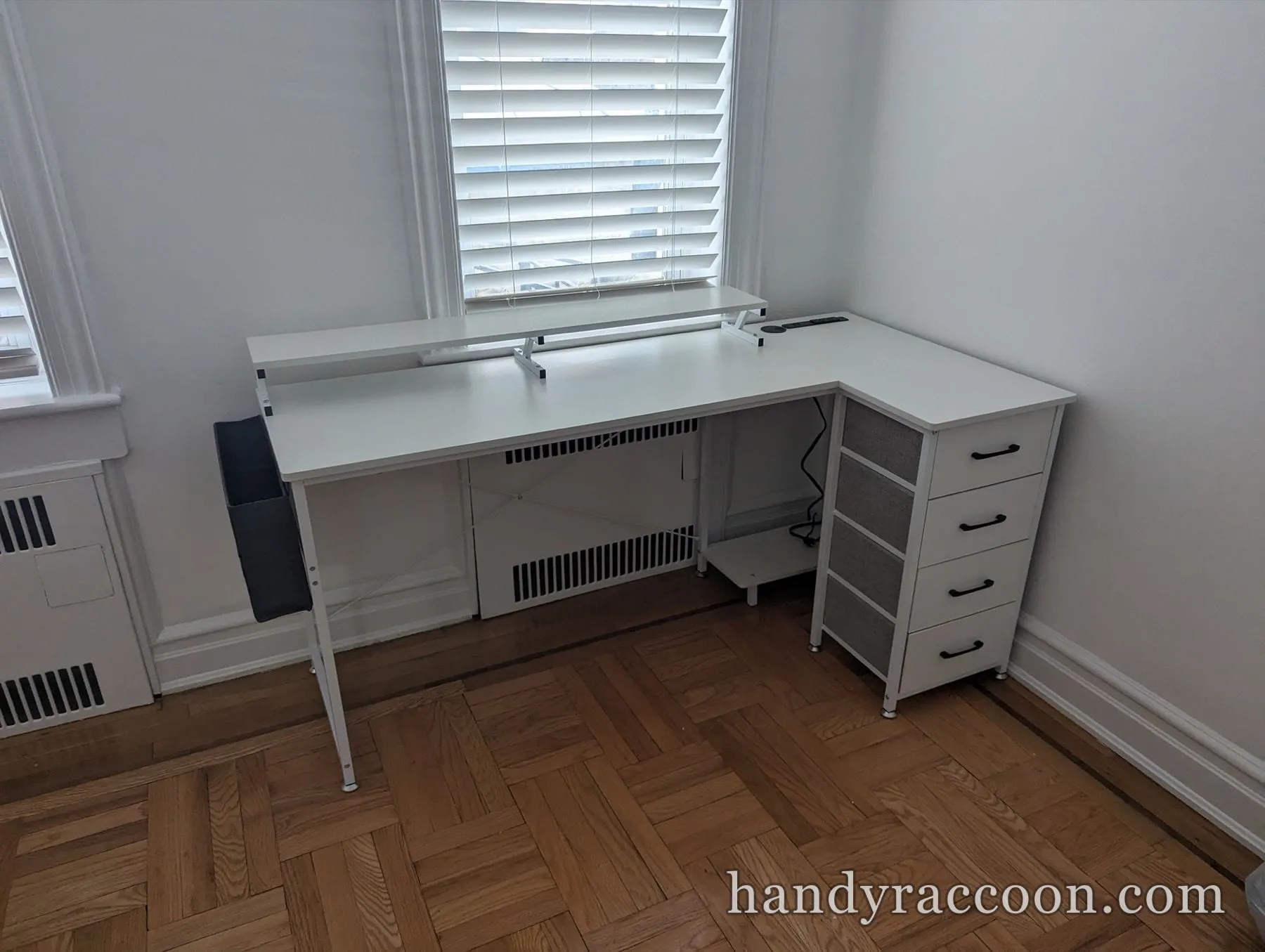 White L-shaped desk with a raised shelf and a white four-drawer storage tower in a corner.