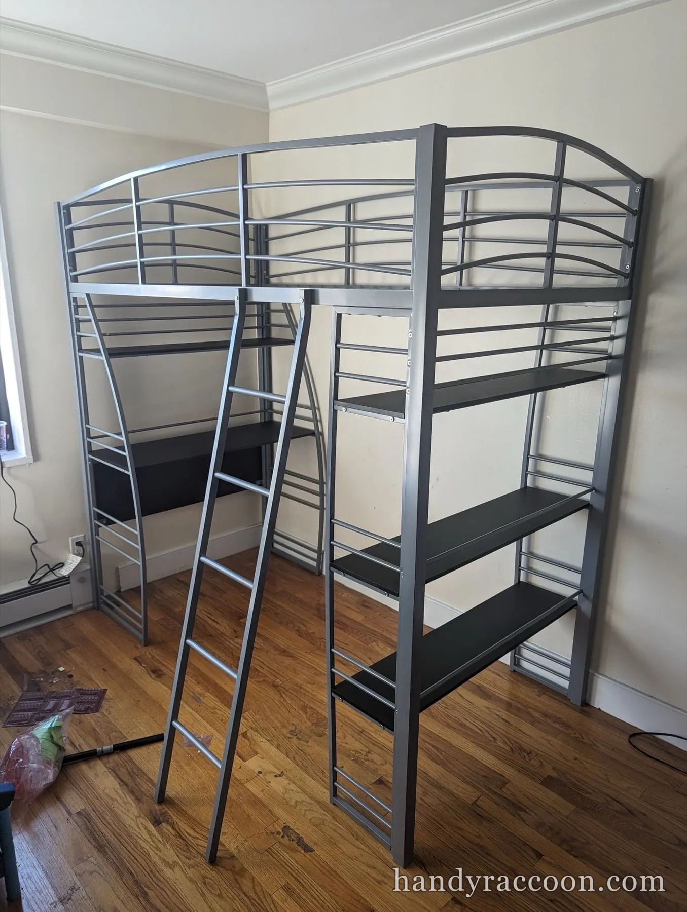Silver metal loft bed frame with an attached desk, shelving and a ladder, no mattress.