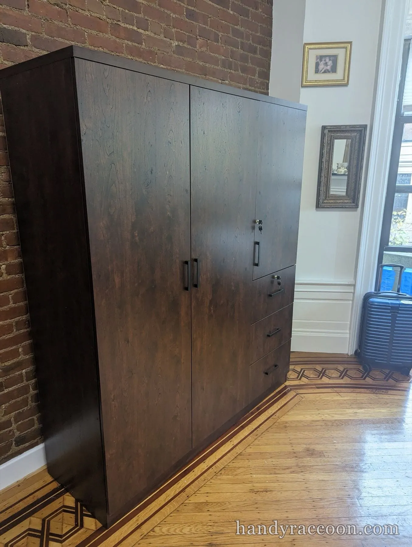 Dark wood wardrobe cabinet with locking doors and drawers on inlaid parquet flooring.