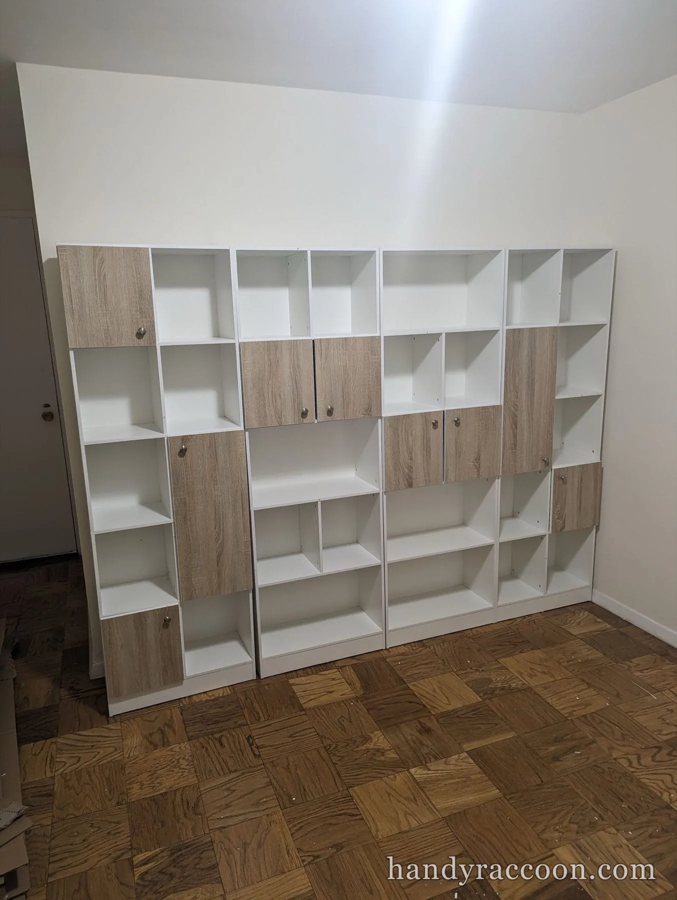 Row of white and oak-front cubby bookshelves lining a wall on parquet flooring.