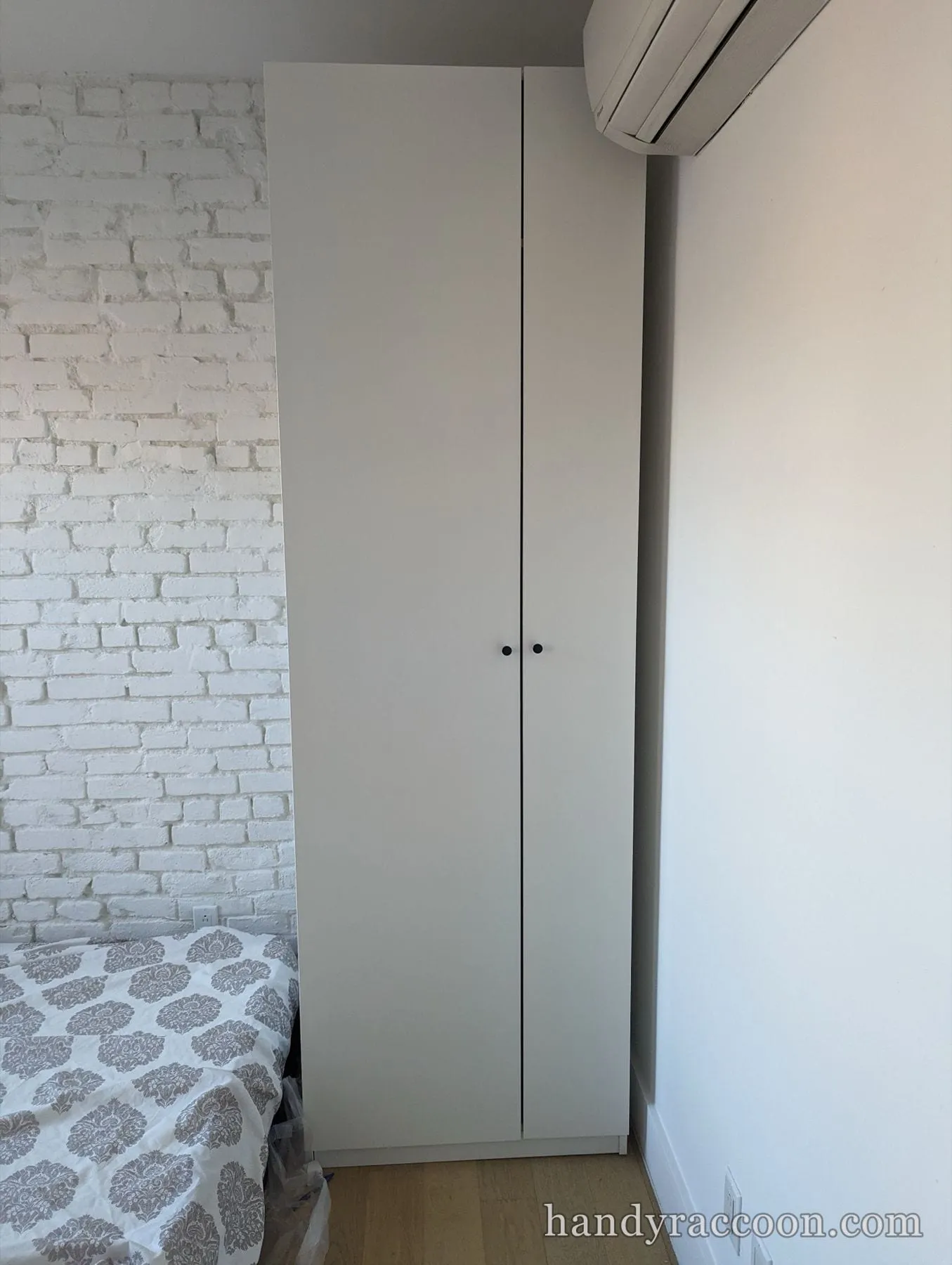 Floor-to-ceiling white wardrobe with round knobs next to a bed and a wall AC unit.