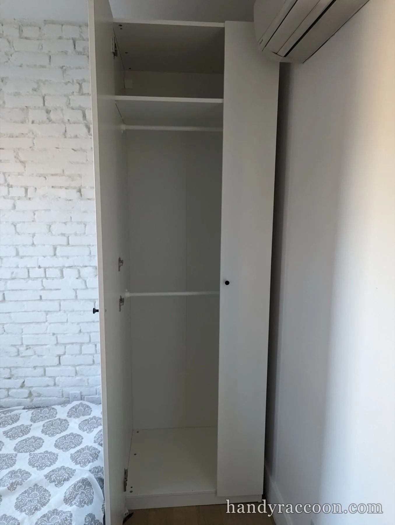 Open white wardrobe showing an empty interior with a clothes rail and a single shelf.