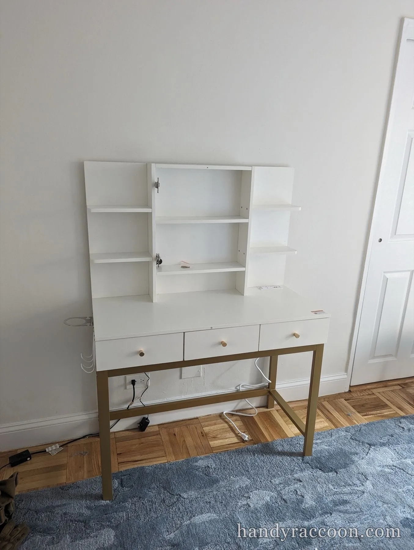 White three-drawer desk with an upper shelf hutch and gold metal legs on a blue rug.
