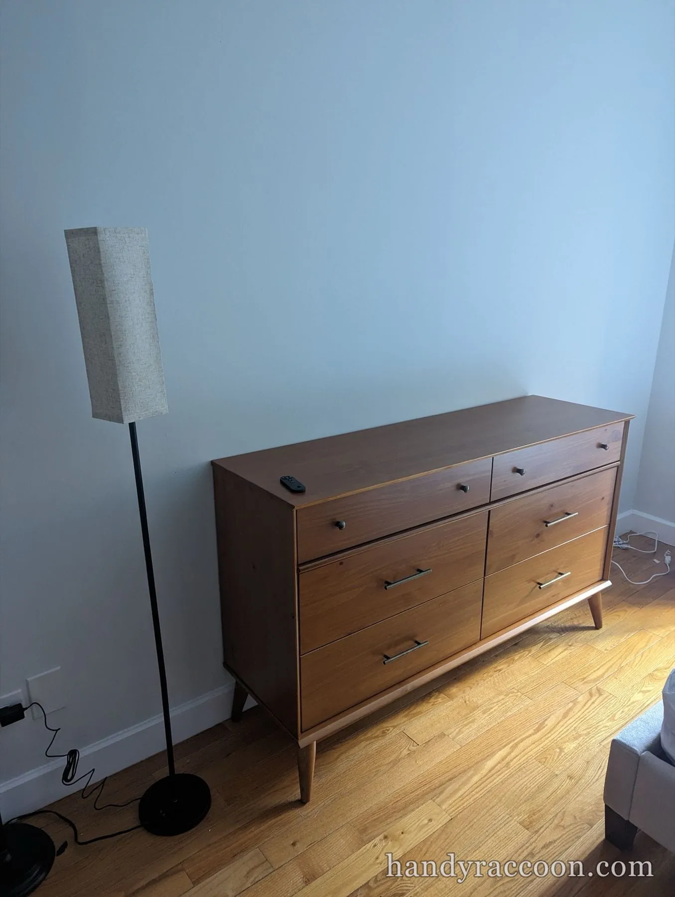 Wood mid-century dresser with six drawers and tapered legs next to a tall floor lamp.