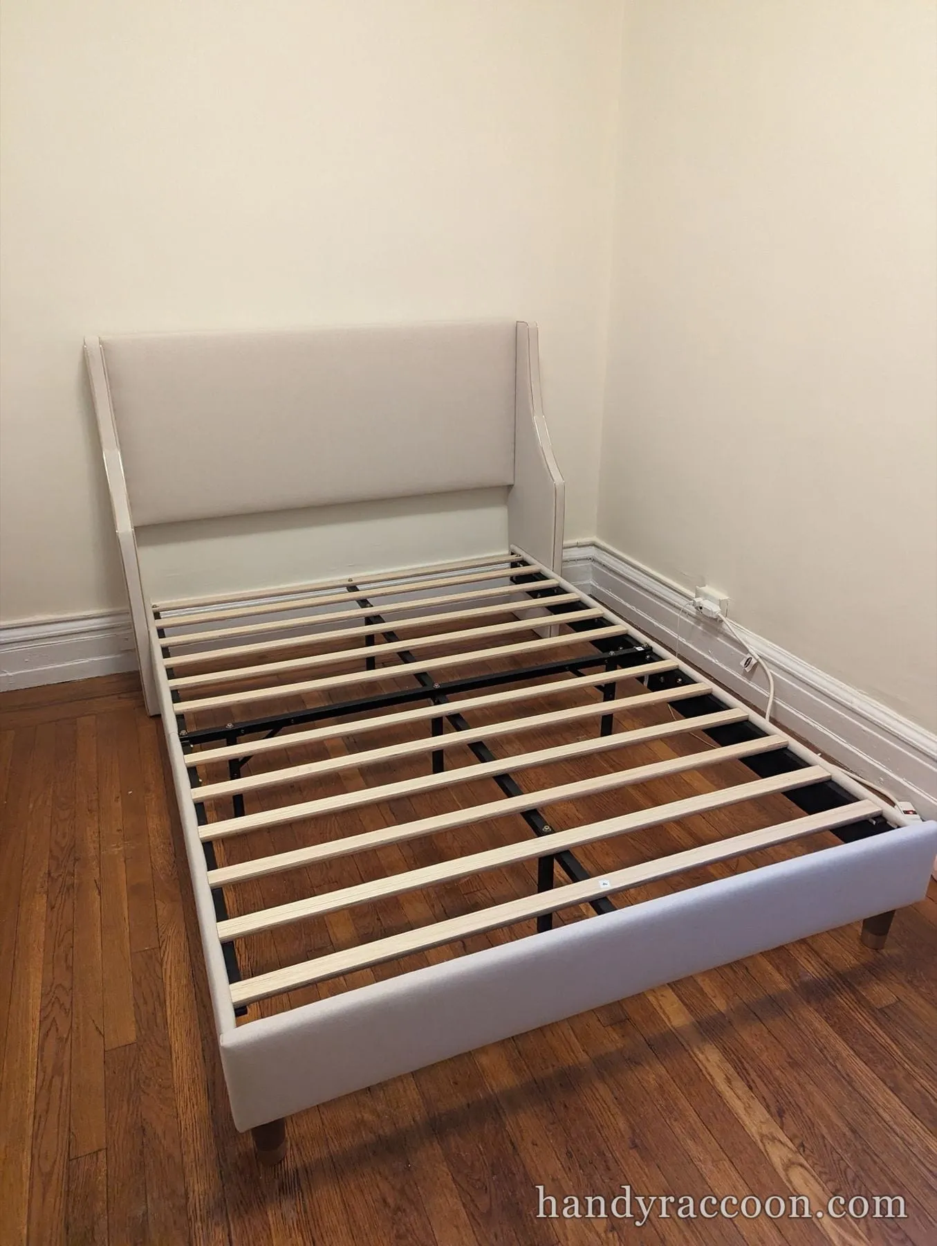 Cream upholstered platform bed frame with a wingback headboard and a wood slat base.