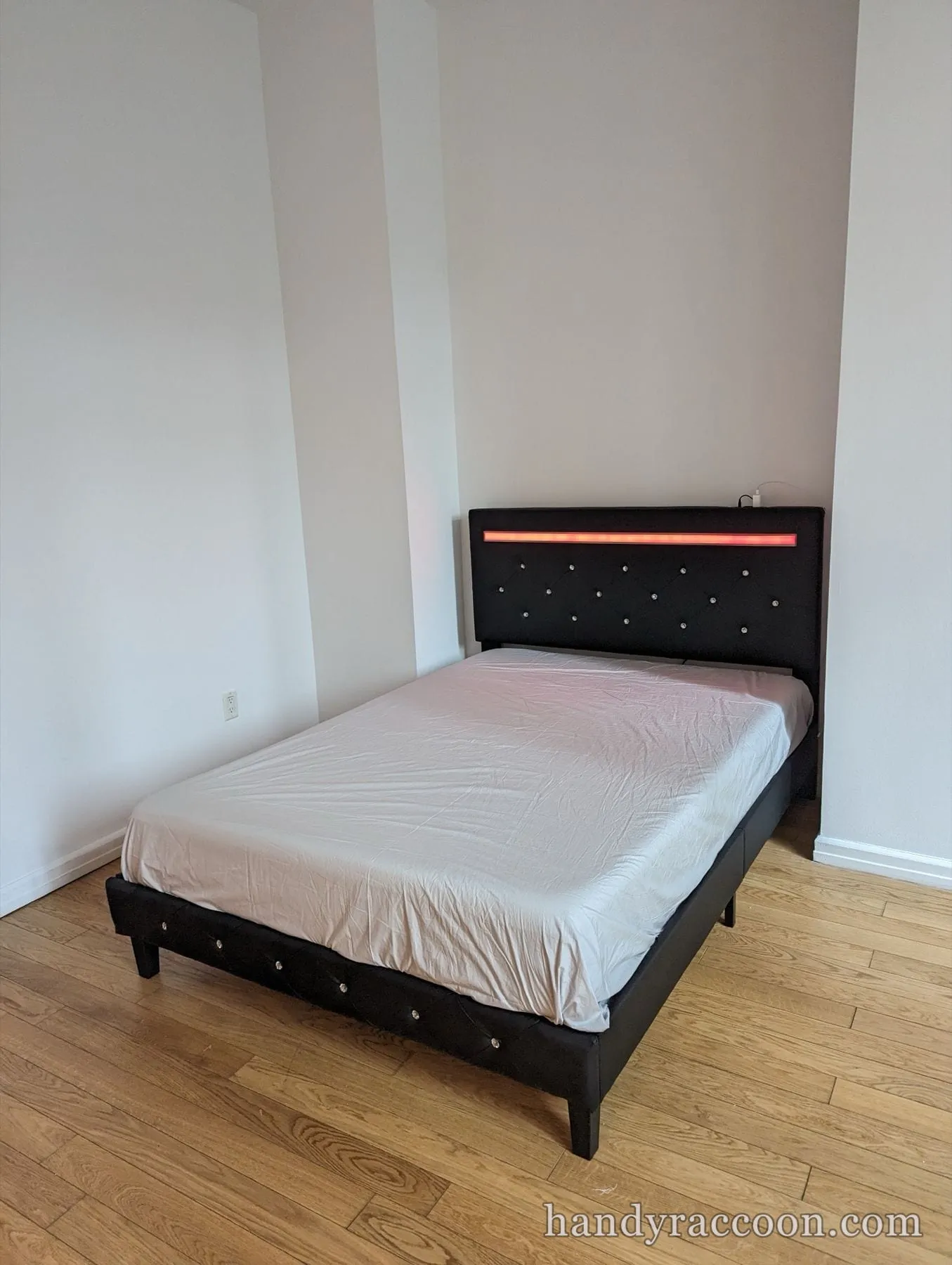 Black upholstered platform bed with a red LED headboard strip and a mattress in place.