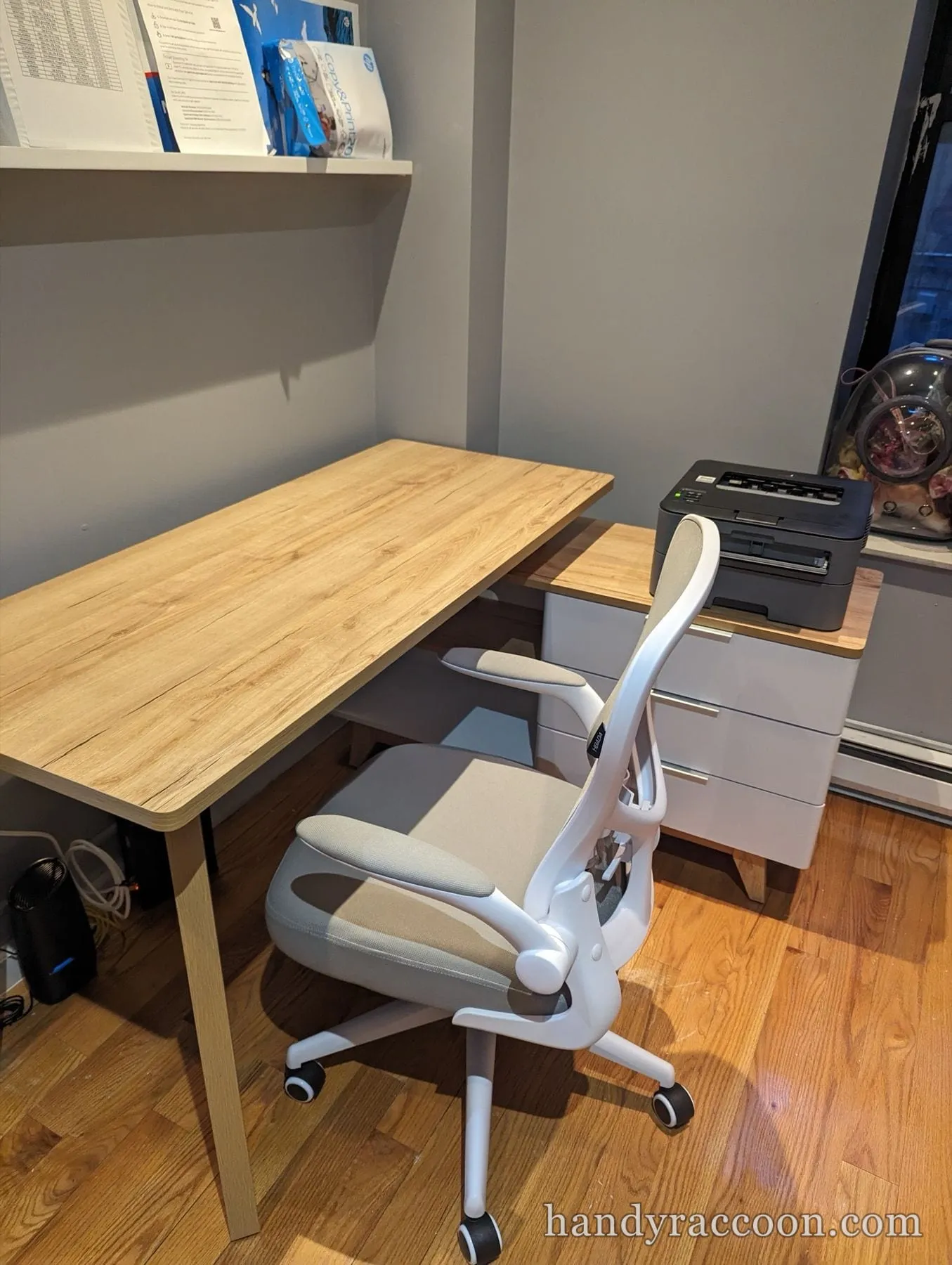 Oak-look desk with a white mesh office chair and a three-drawer unit holding a printer.