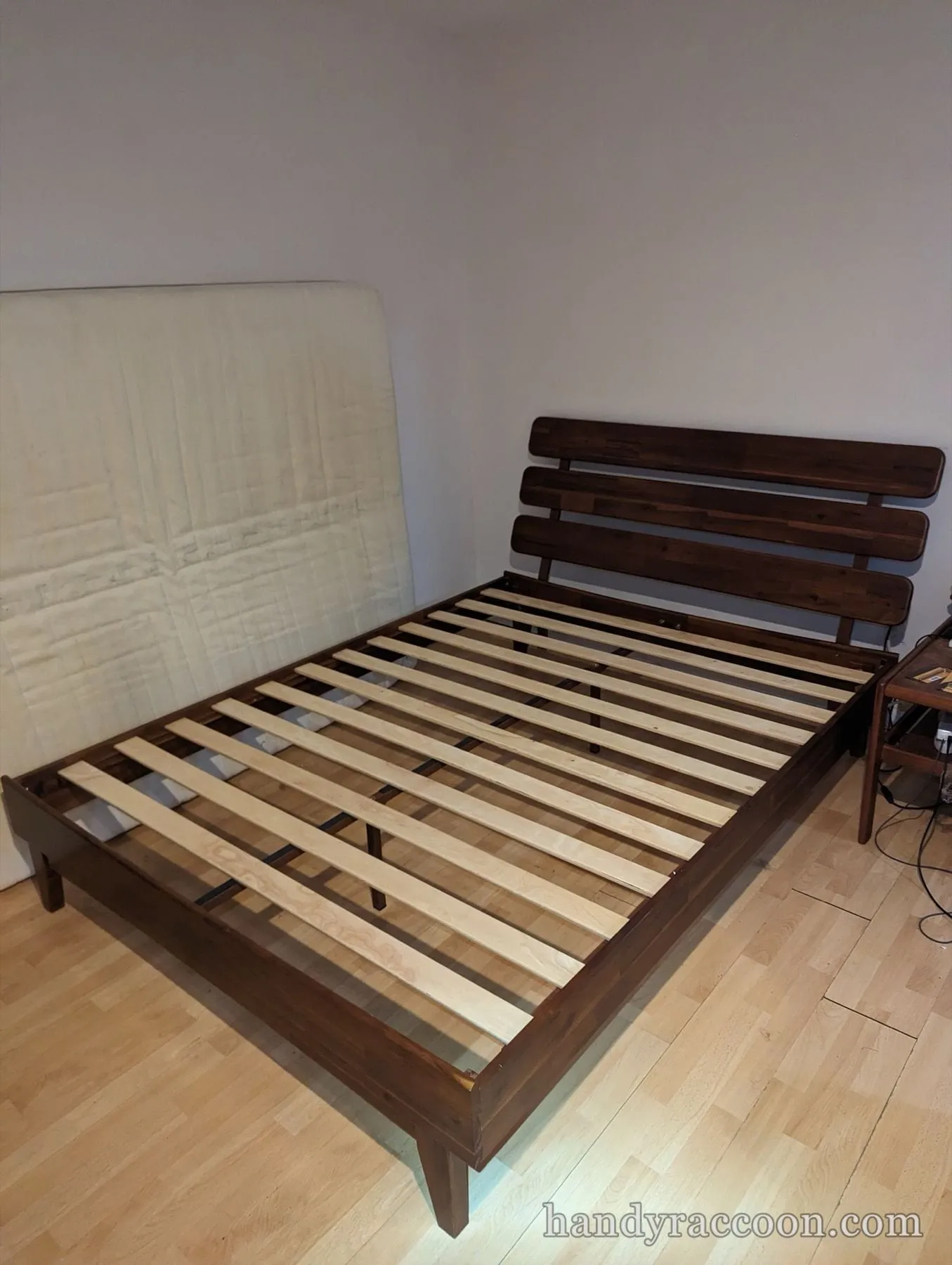 Brown wood platform bed frame with a horizontal slat headboard and bare support slats.