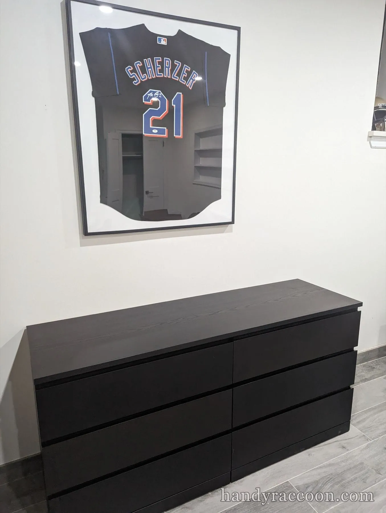 Long black six-drawer dresser against a white wall under a framed signed baseball jersey.
