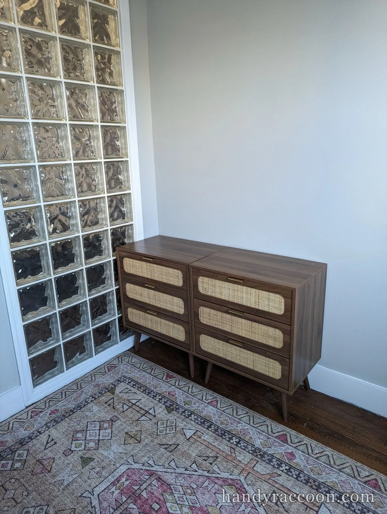 Two matching walnut dressers with cane drawer fronts on a patterned rug by a glass block wall.