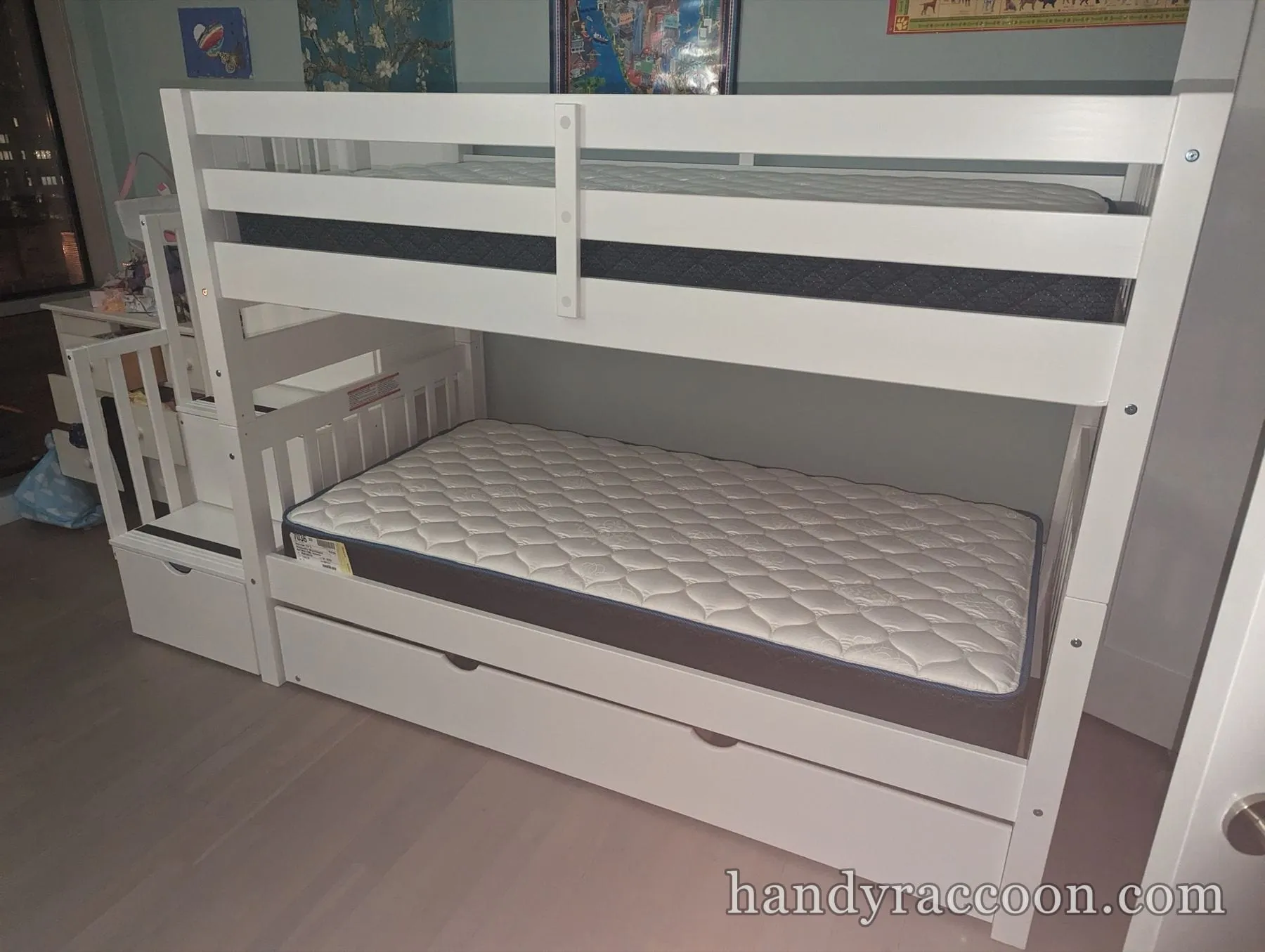 White twin-over-twin bunk bed with a step staircase and pull-out trundle in a kids room.