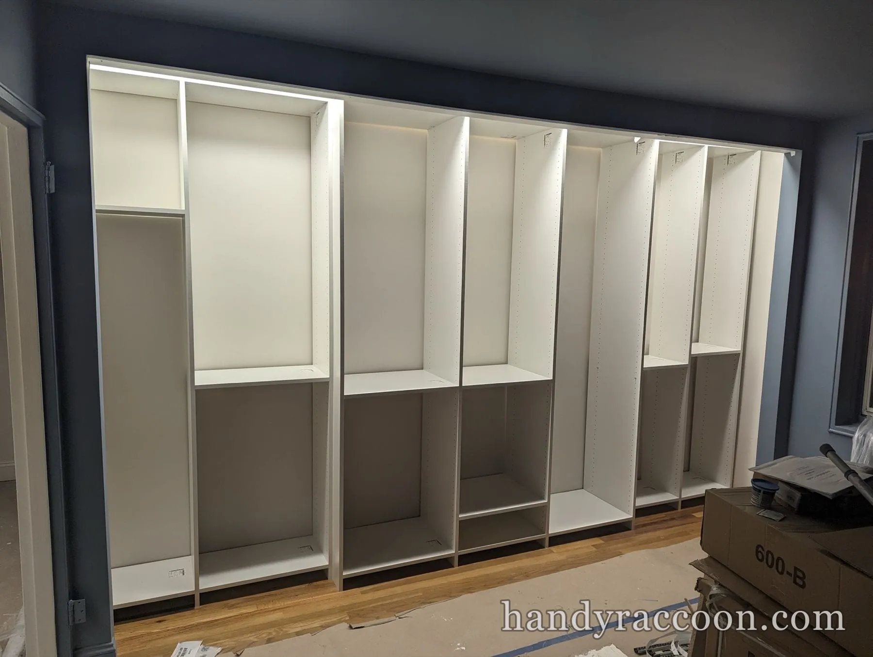 Row of tall empty white built-in closet cabinets assembled against a dark blue wall mid-renovation.