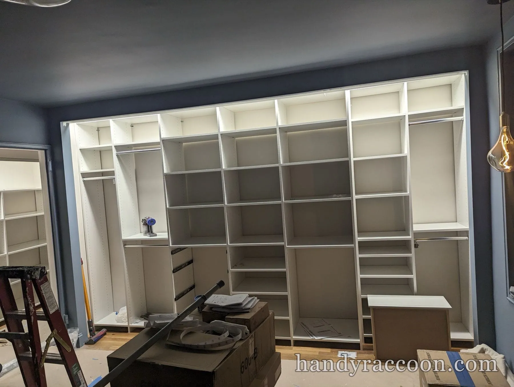 Large white built-in closet with lit interior, hanging rods and shelves along a dark blue wall.