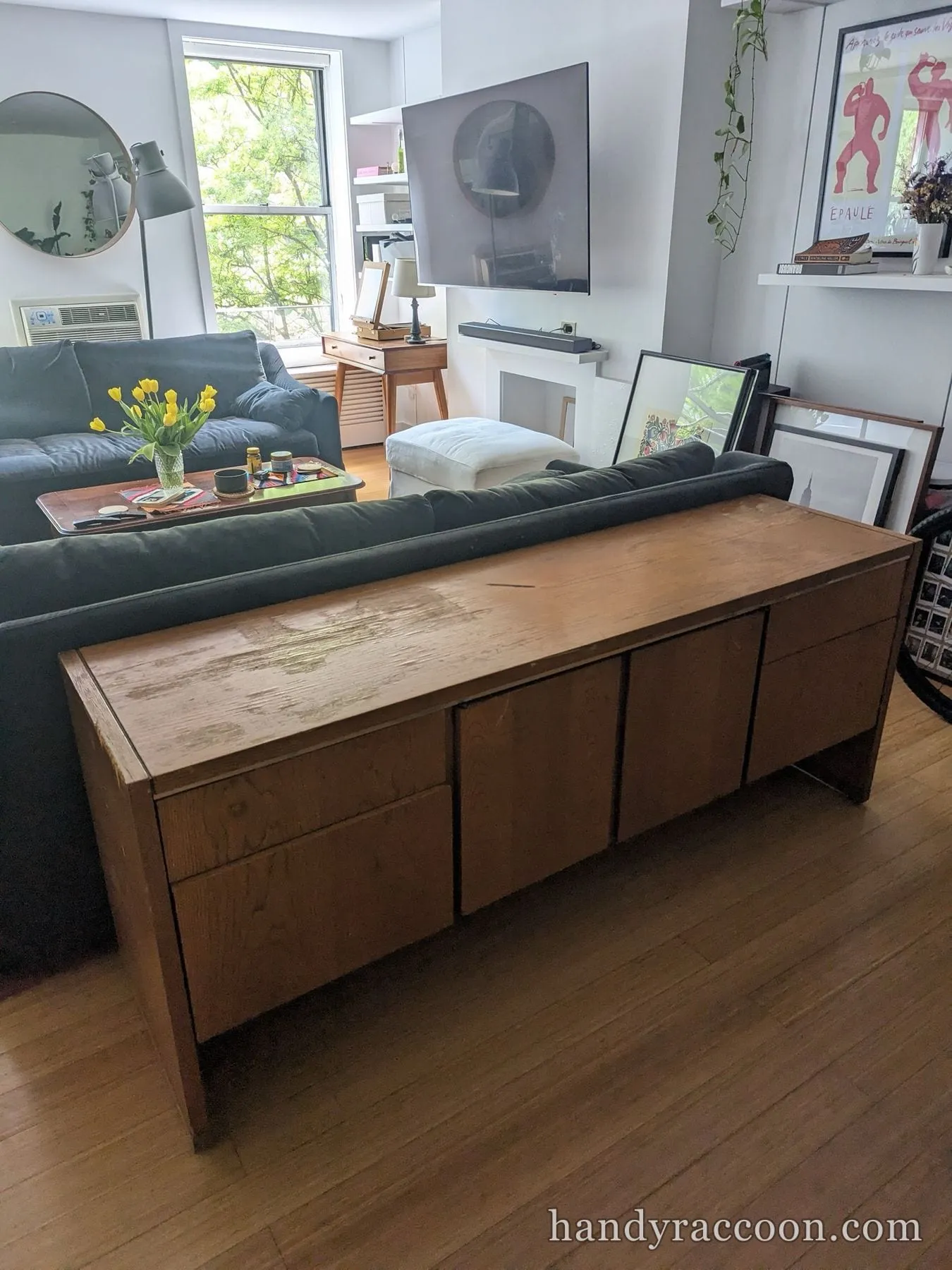 Assembled wooden storage credenza with drawers and doors behind a green living room sofa.