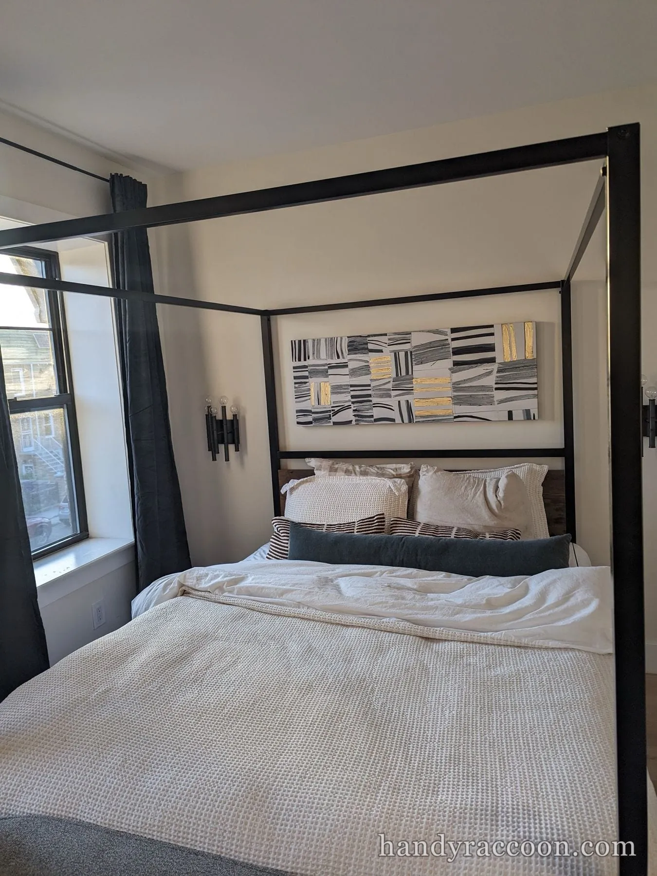 Black metal four-poster canopy bed frame assembled and made up beneath framed wall art.