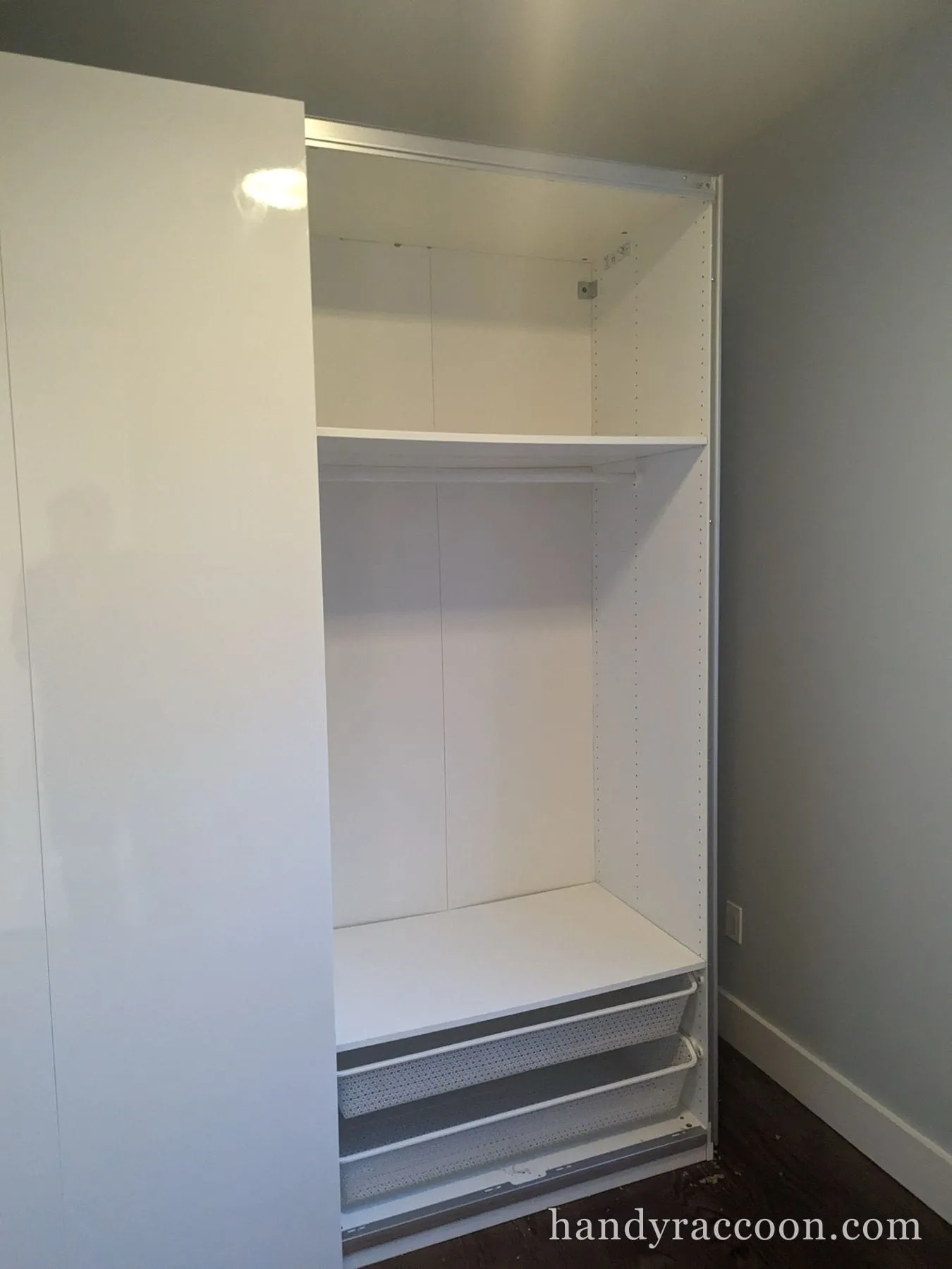 White wardrobe interior with a shelf, hanging rod, and pull-out wire baskets.