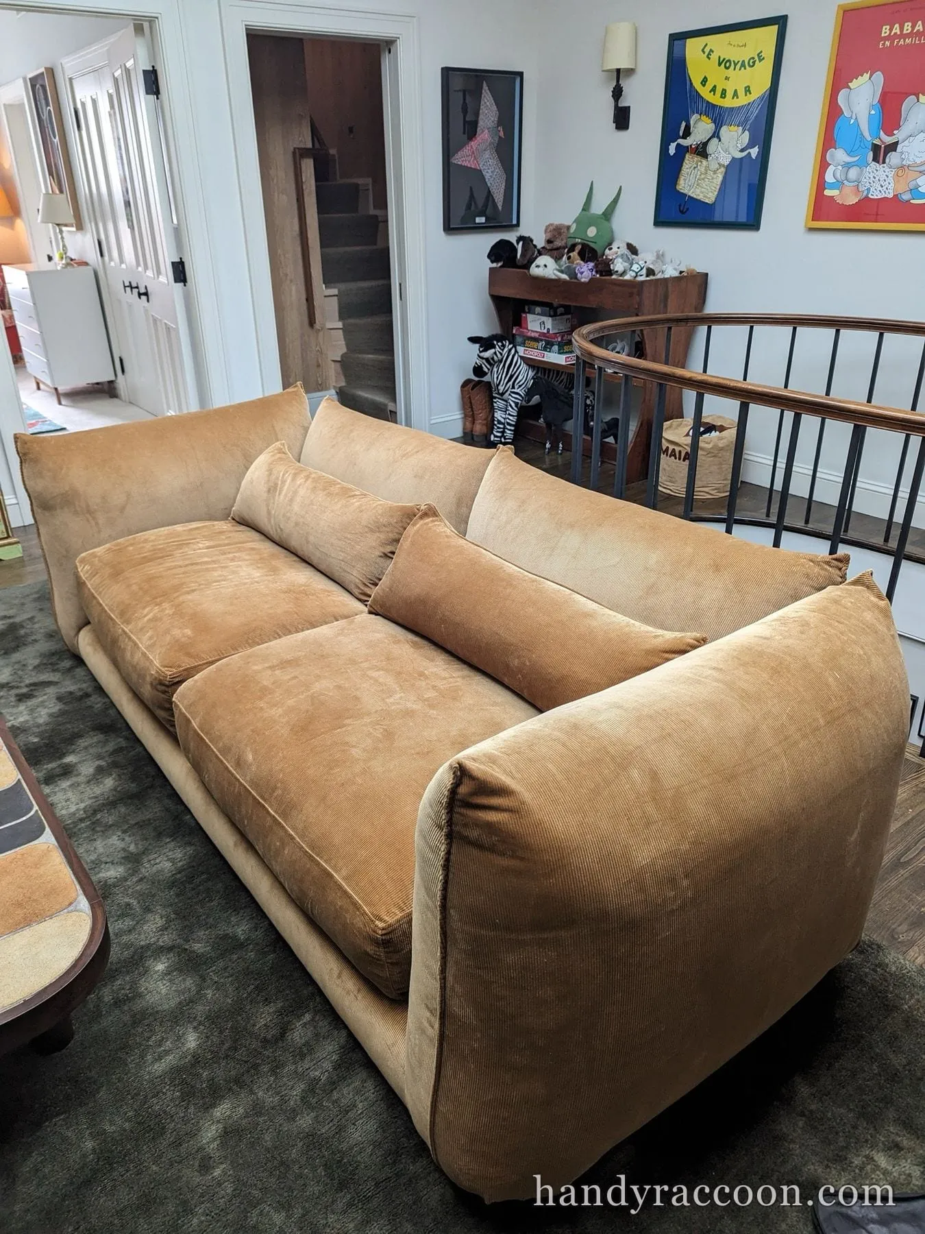 Large tan corduroy three-cushion sofa with bolster pillows in a living room by a staircase railing.
