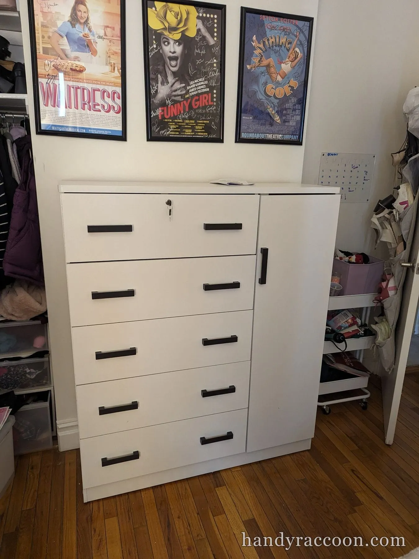 White chest of drawers with a side cabinet door in a room with framed theater posters above.