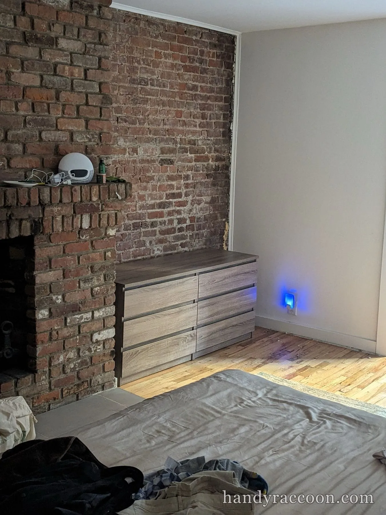 Gray wood-tone six-drawer double dresser against an exposed brick wall next to a fireplace.