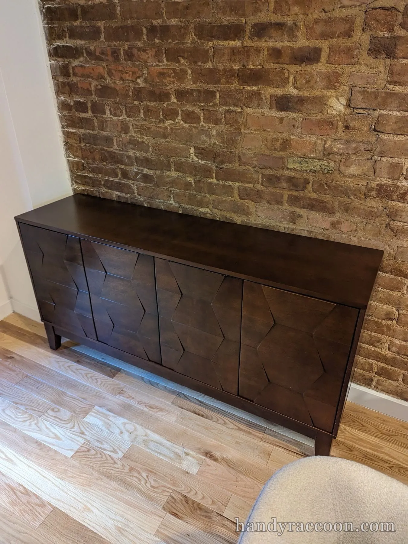 Dark brown sideboard with geometric faceted cabinet doors along an exposed brick wall.