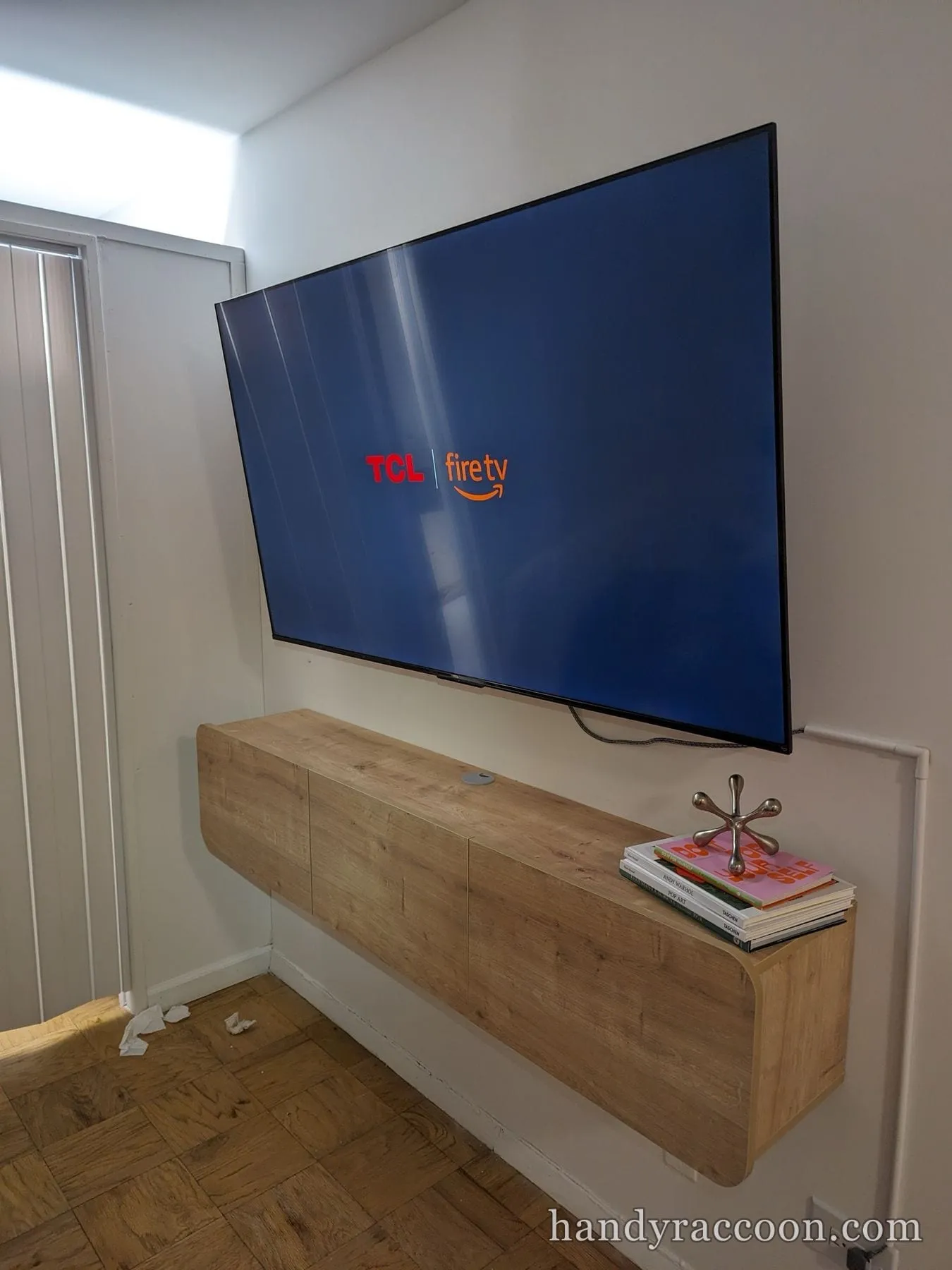 Large flat-screen TV mounted above a floating wood console, boot logo on screen.