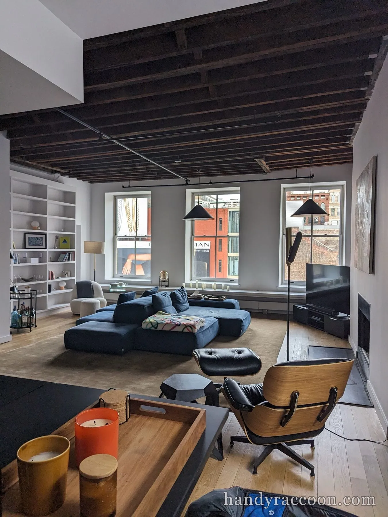 Blue modular sectional sofa and a leather lounge chair in a loft with an exposed wood beam ceiling.
