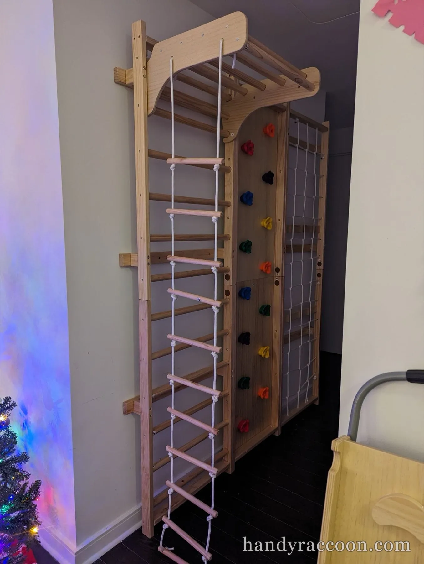 Wall-mounted wooden gymnastic bars with a rope ladder, climbing wall and net in a room.