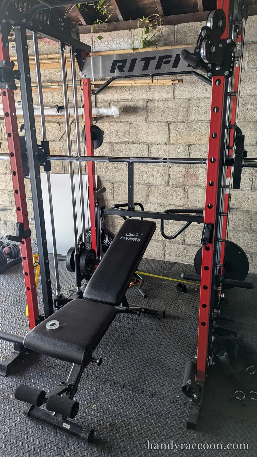 Red and black Smith machine power rack with a black adjustable bench in a garage.