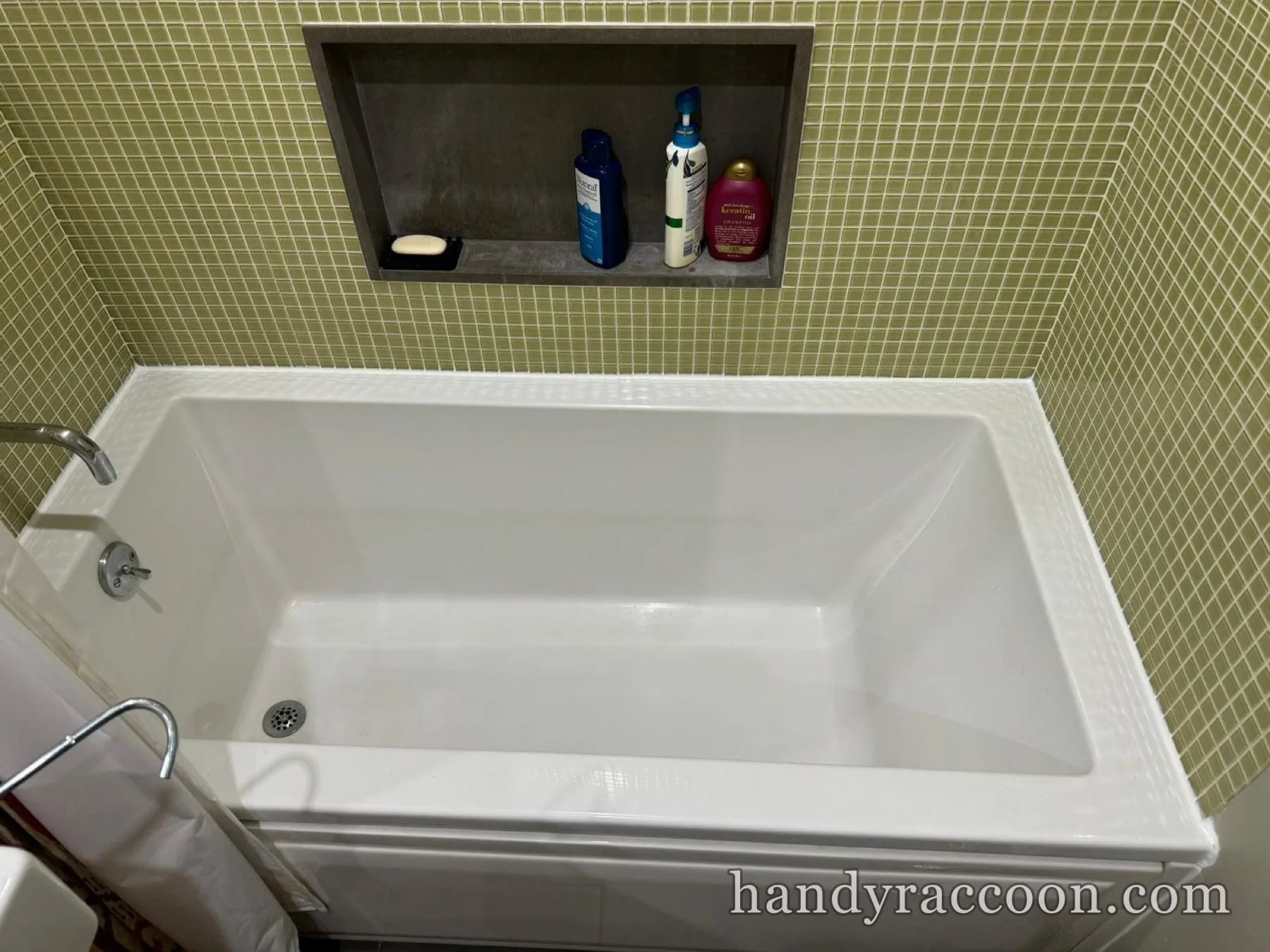 White rectangular drop-in bathtub with green mosaic tile wall and a tiled storage niche.
