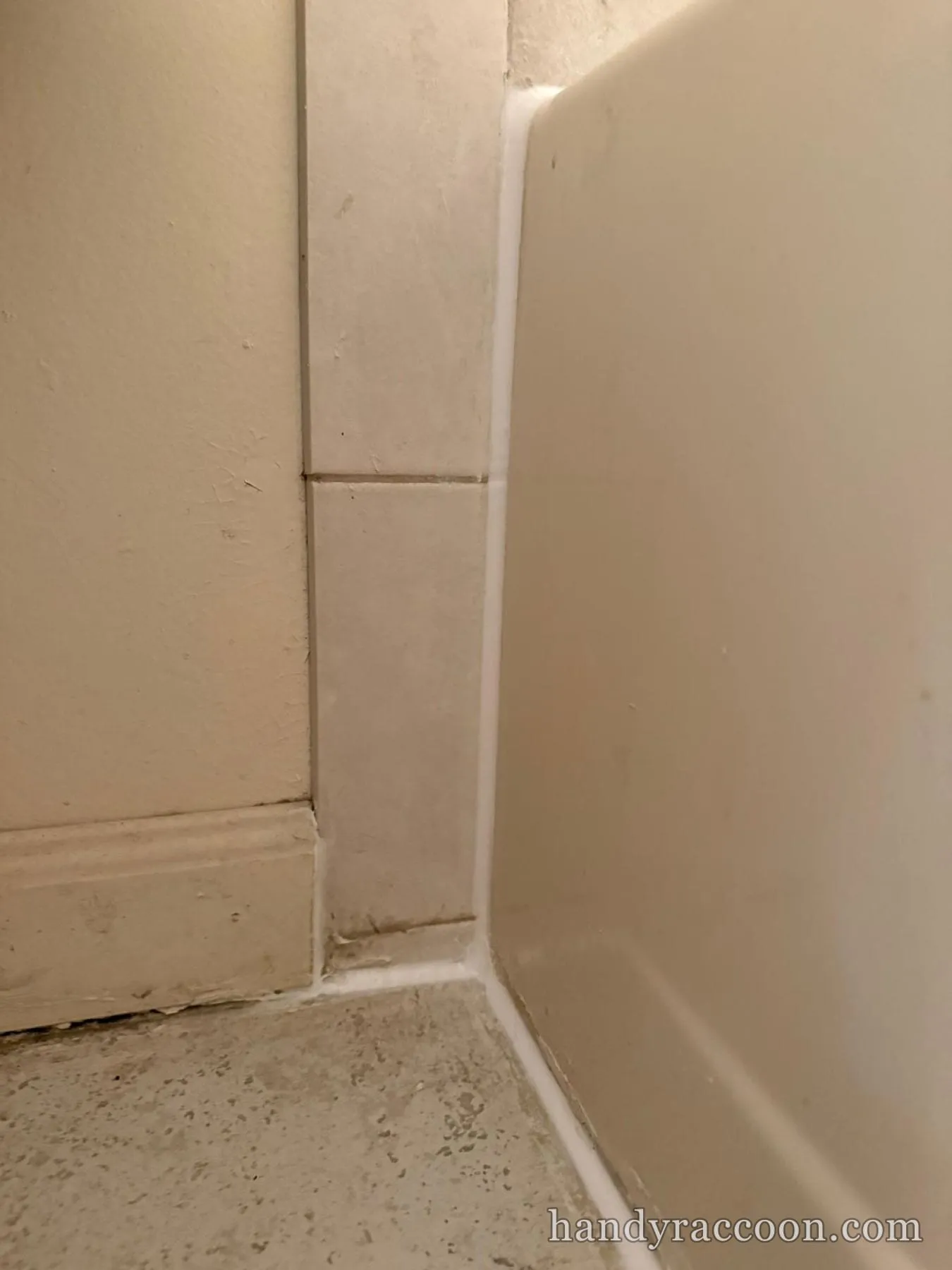 Neat white caulk line sealing the corner where a bathtub meets a tiled wall and floor.