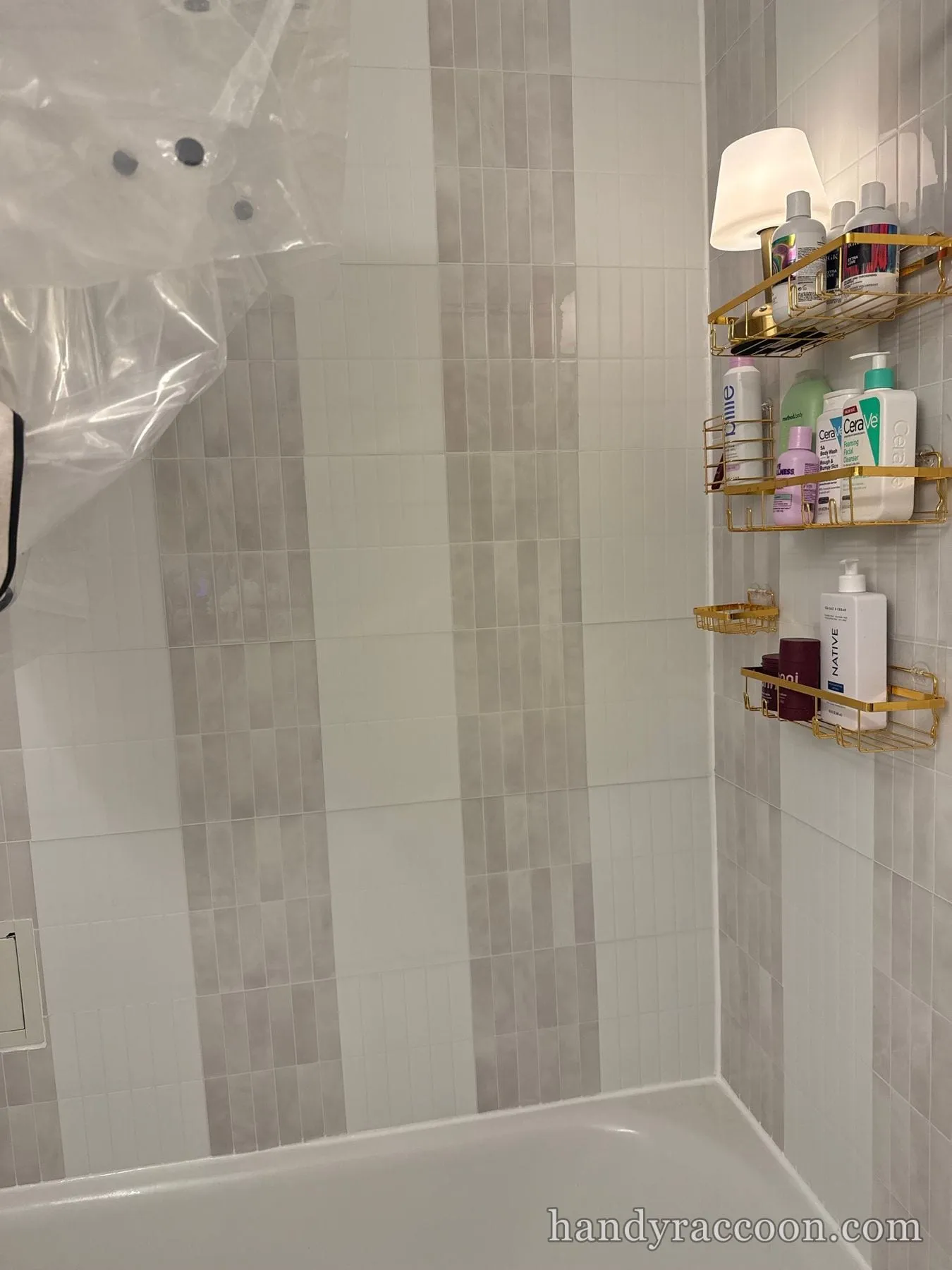 Vertical stacked gray and white tile shower wall with gold caddies of toiletries.