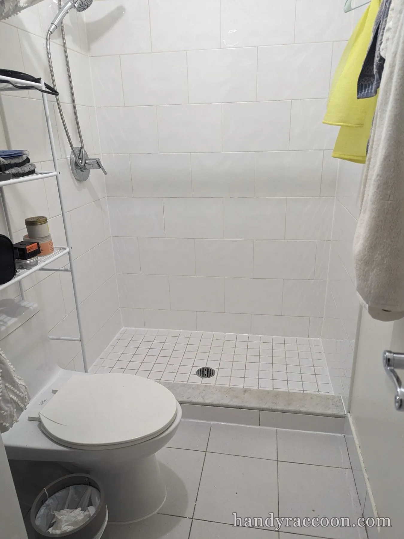 White tile walk-in shower with handheld fixture, mosaic floor, drain and marble threshold.