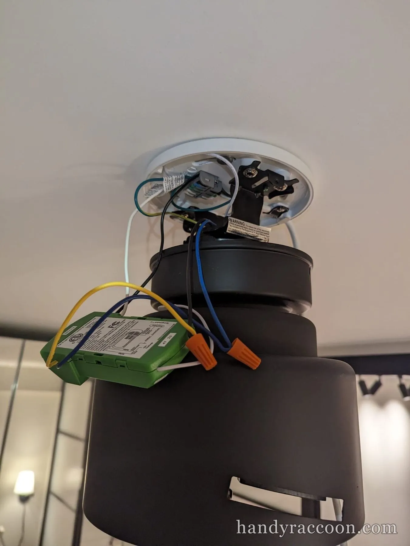 Underside of a black ceiling fan being wired to a ceiling bracket with a green receiver module.