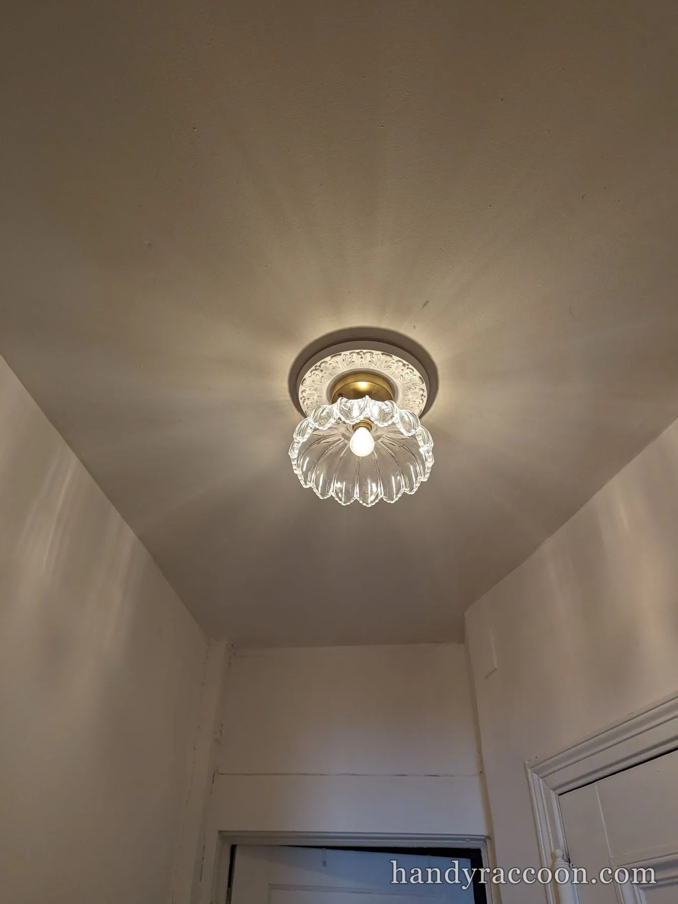 Lit clear scalloped glass flush-mount ceiling light on a decorative round ceiling medallion.