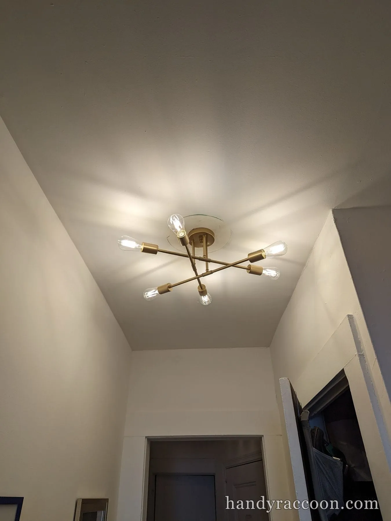 Gold six-arm semi-flush ceiling light with exposed Edison bulbs lit in a hallway.