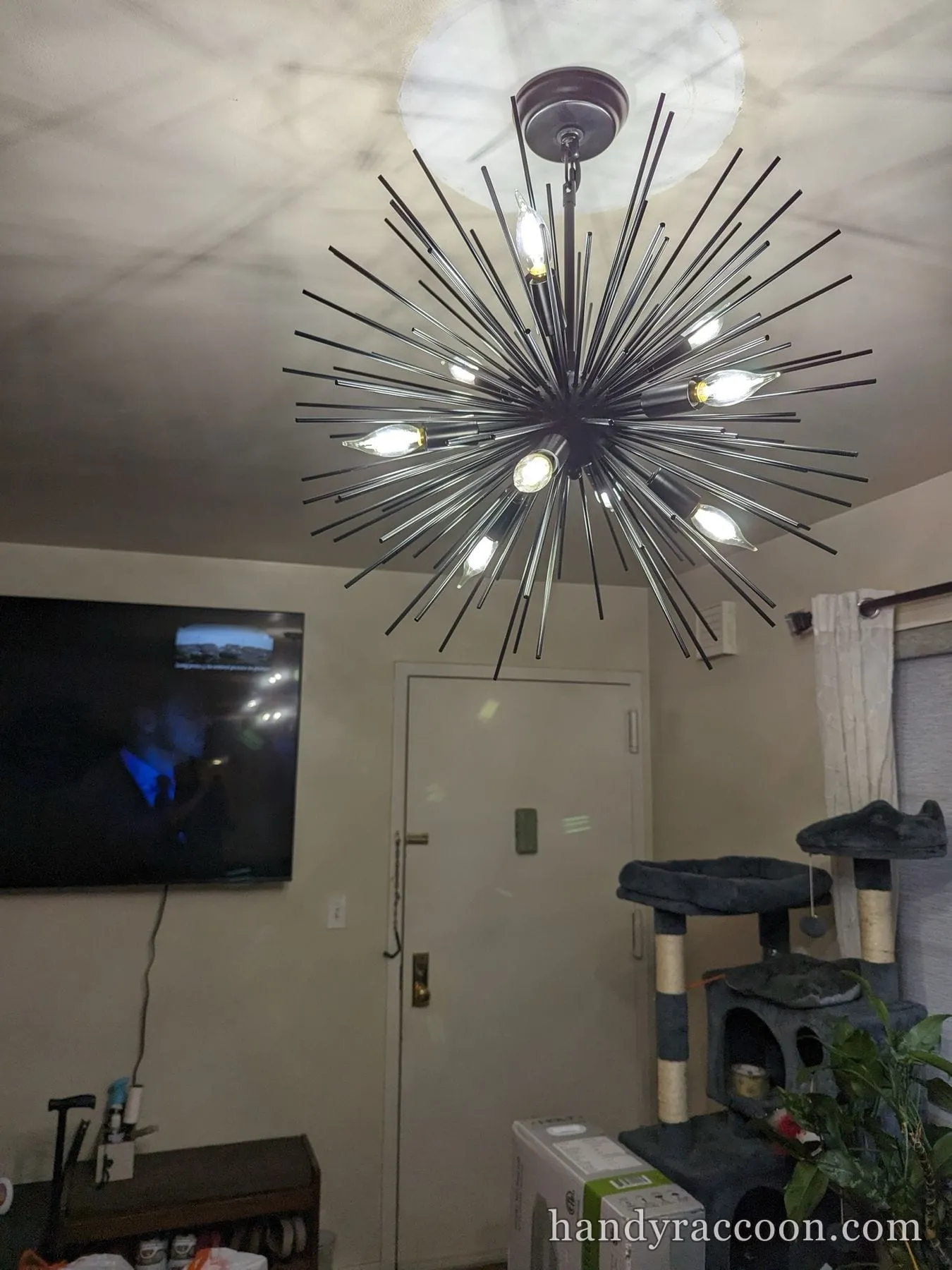 Black spiked starburst chandelier with lit candelabra bulbs in a living room.