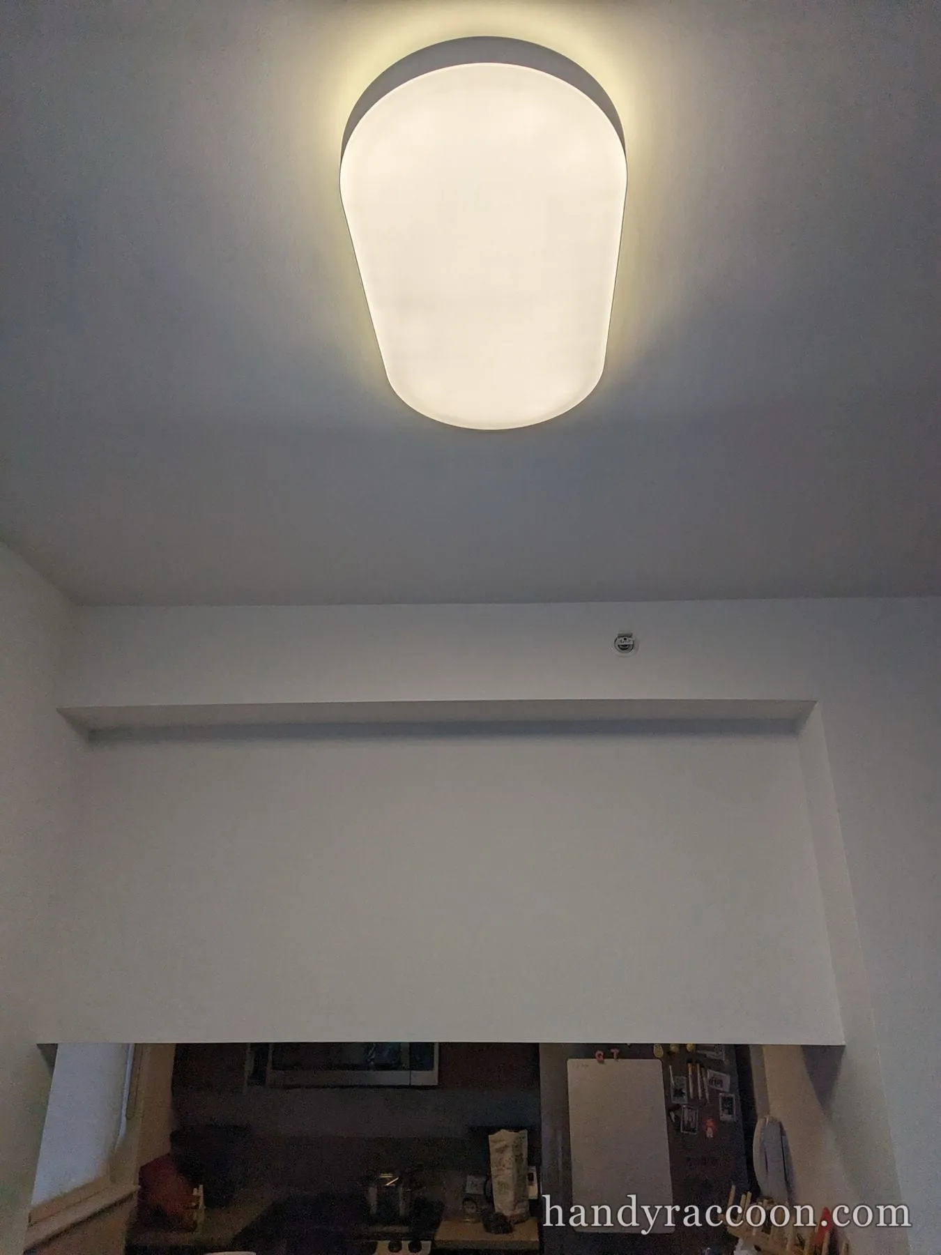 White oval dome flush-mount ceiling light glowing above a room opening.