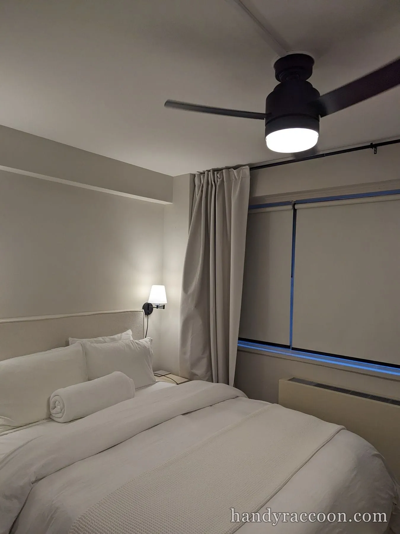 Black three-blade ceiling fan with a lit light kit installed above a bedroom.